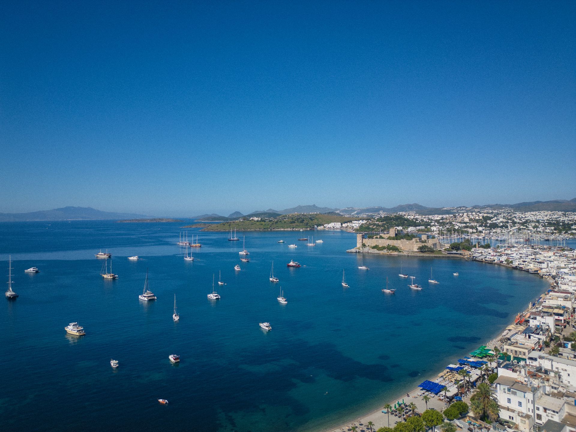 Manzara Boutique Hotel | Aerial view of a coastal bay with many sailboats, blue water, sandy beach