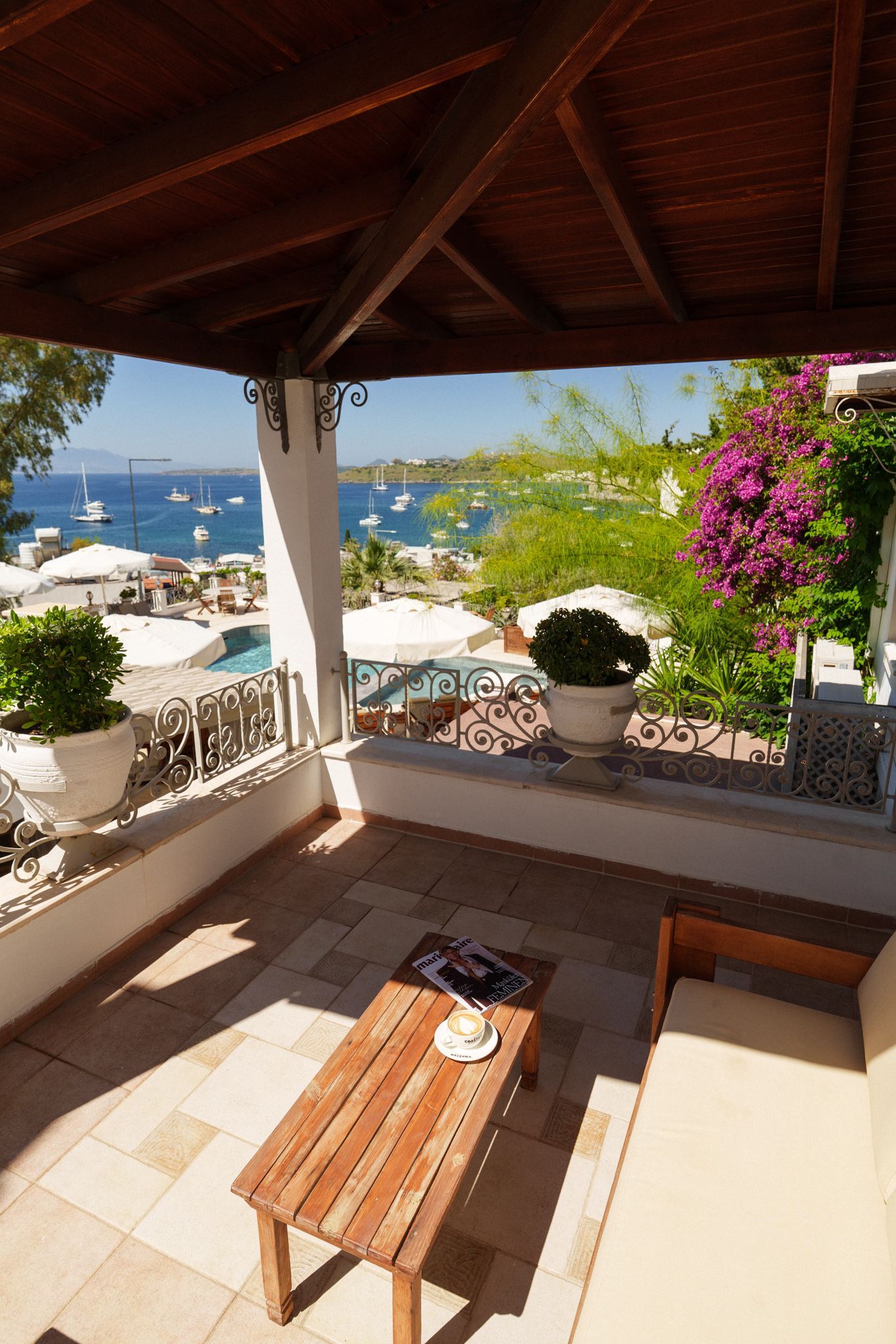Manzara Boutique Hotel | Shaded terrace with wicker bench, potted plants, and a sea view beyond white railings.