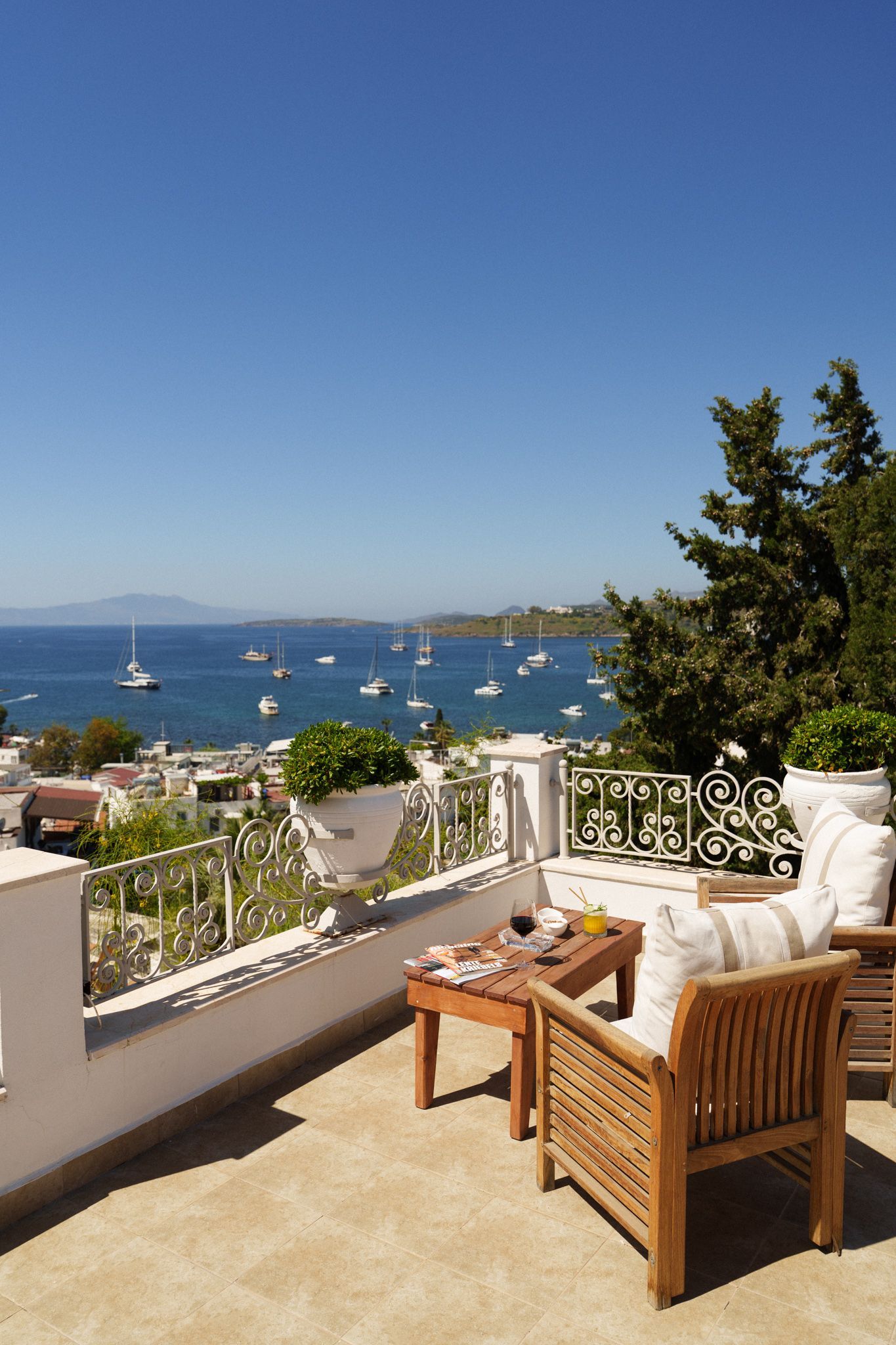 Manzara Boutique Hotel | Sunny patio with wicker chairs overlooking a blue bay with sailboats and distant hills.