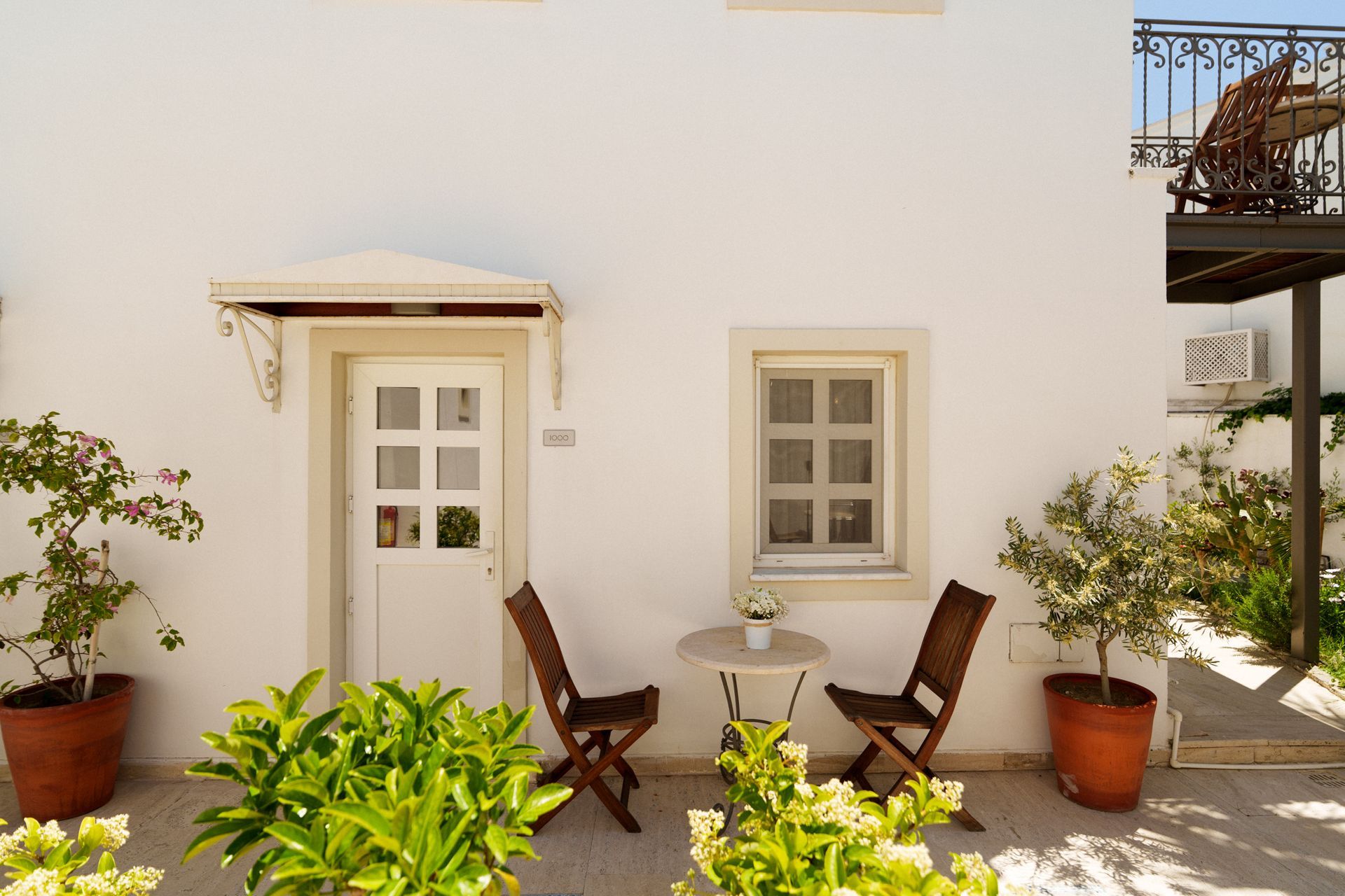 Manzara Boutique Hotel |Sunlit patio with white wall, door, window, two wooden chairs, and potted plants.