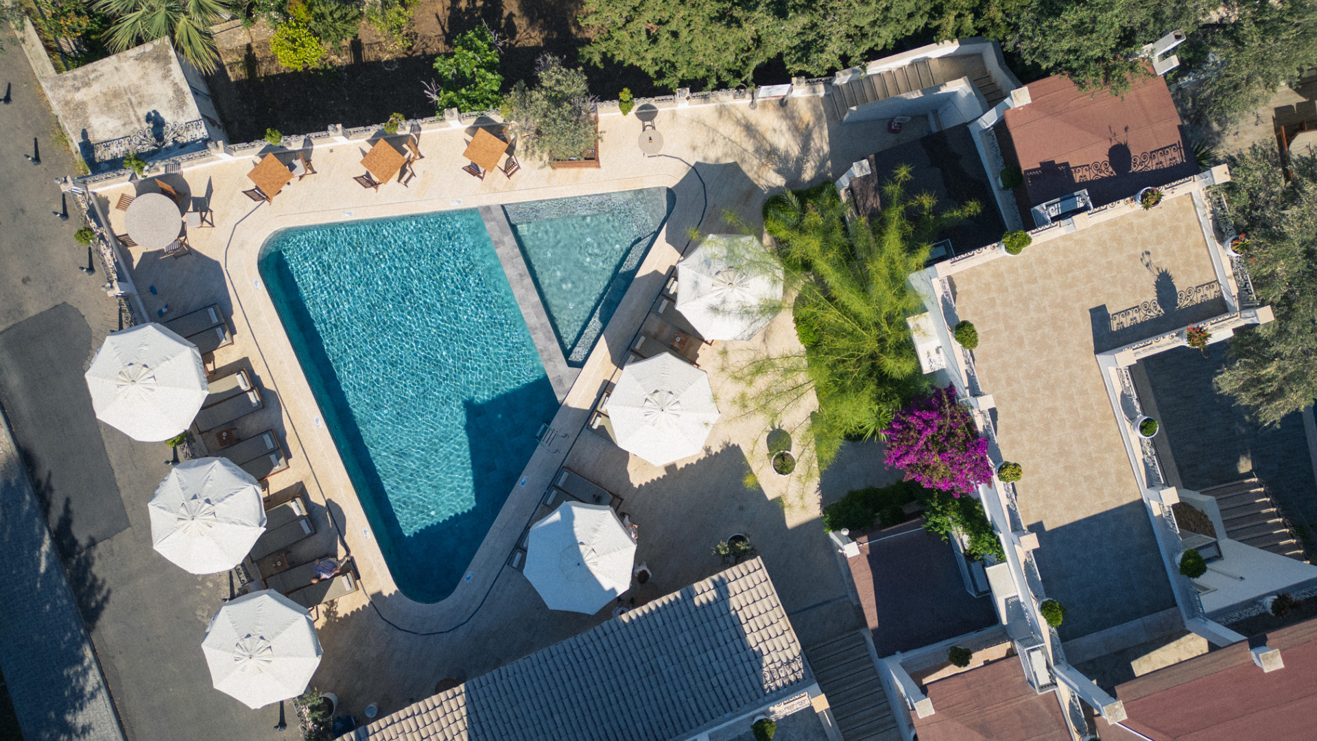 Manzara Boutique Hotel |Aerial view of a turquoise resort pool surrounded, lounge chairs, and greenery.