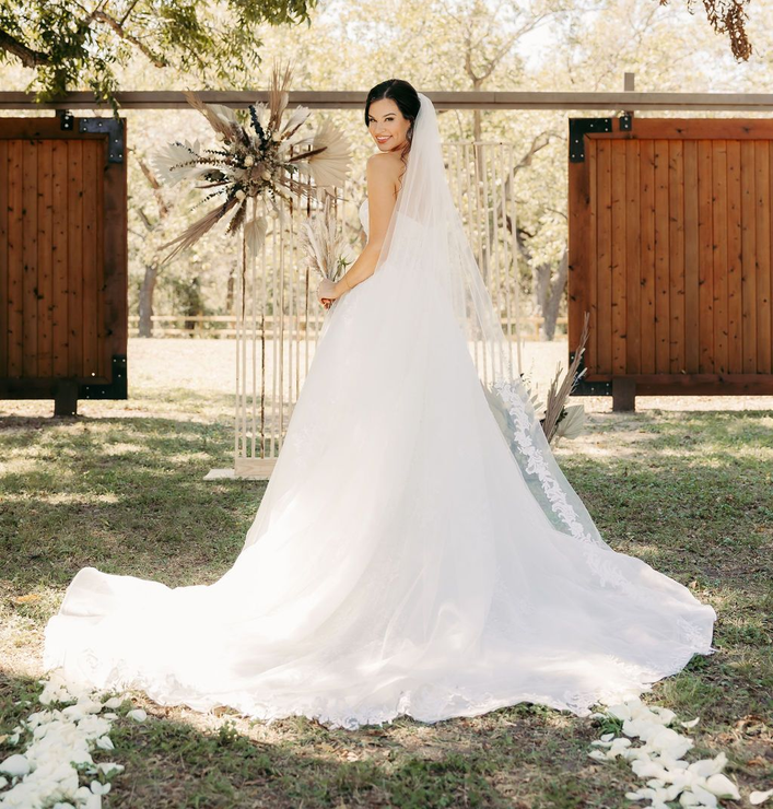 A bride in a wedding dress and veil is standing in the grass.