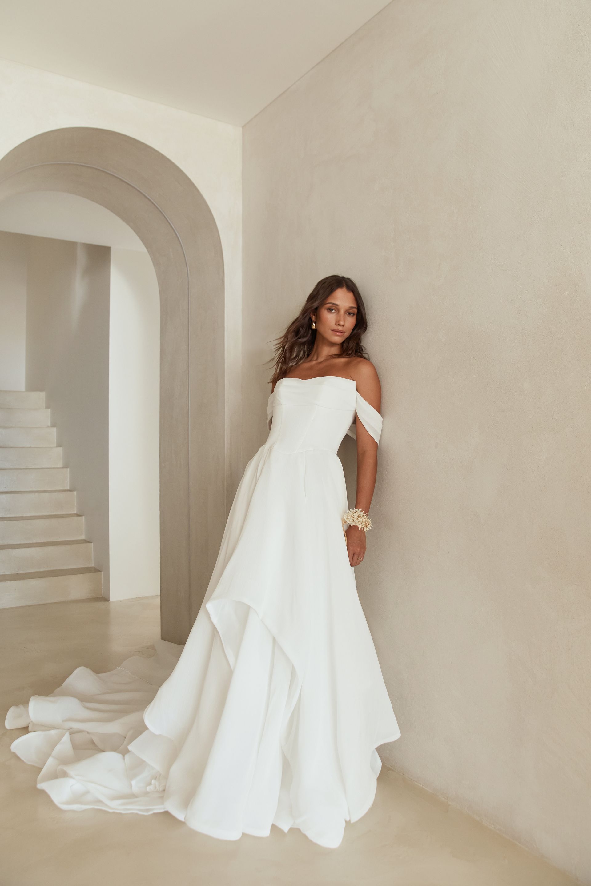 Woman in a white strapless gown posing beside an arched doorway in a bright, minimalist room
