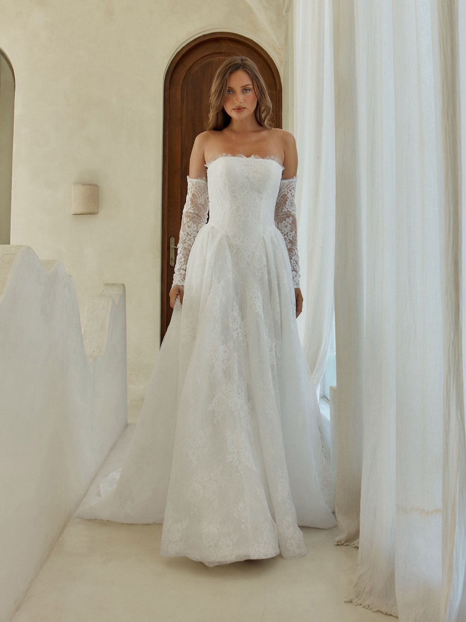 A woman in a white wedding dress is standing in front of a fireplace.