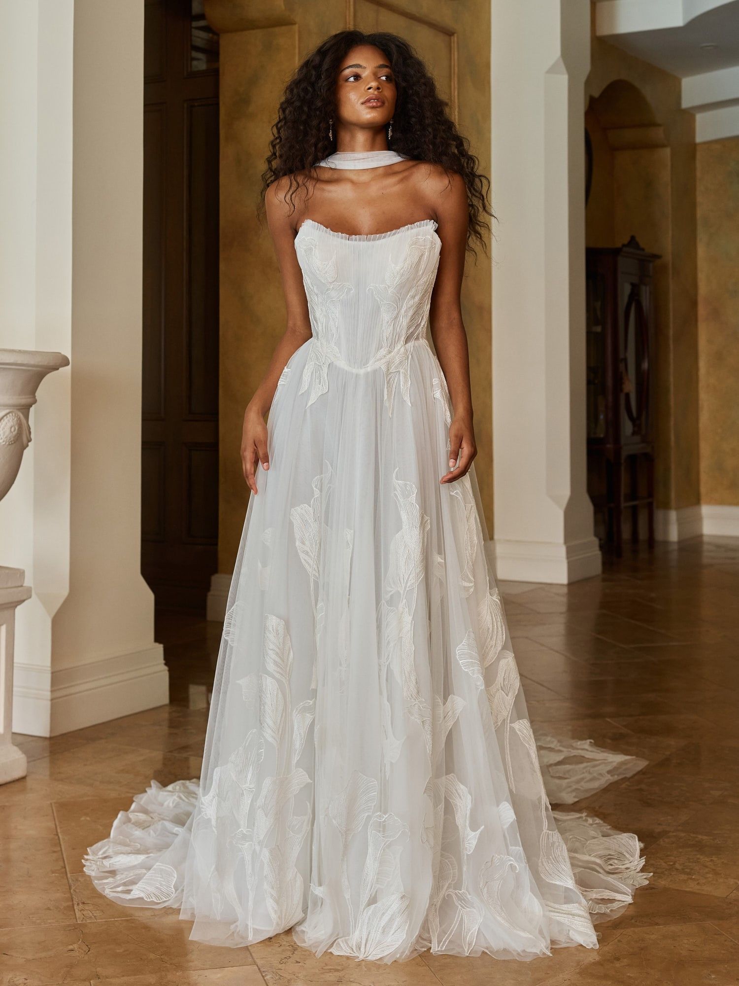 A woman in a white wedding dress is standing in a room with arches.