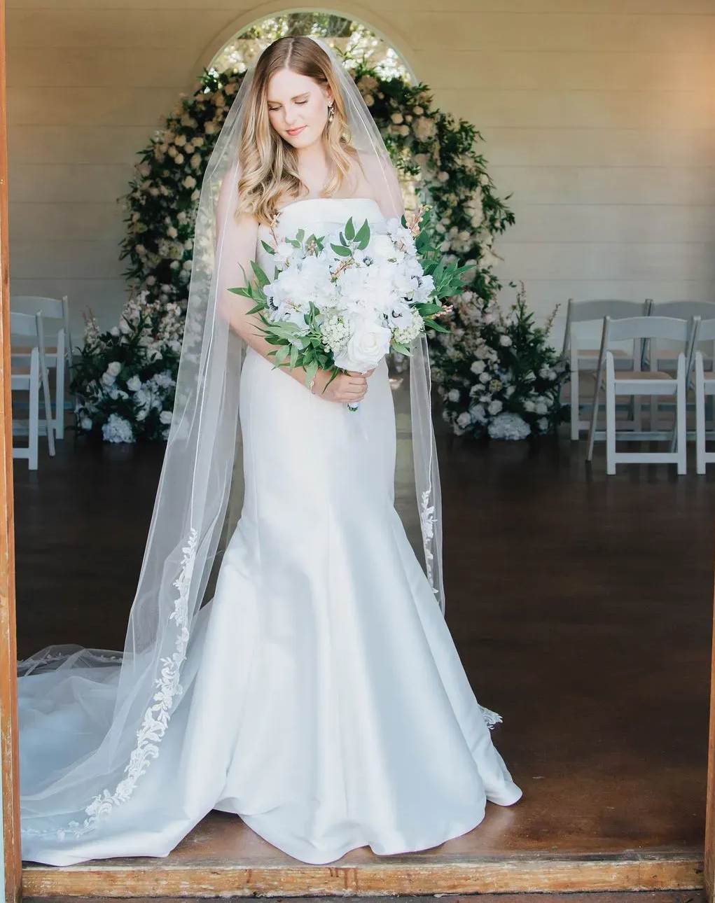 The bride is wearing a long veil and holding a bouquet of flowers.