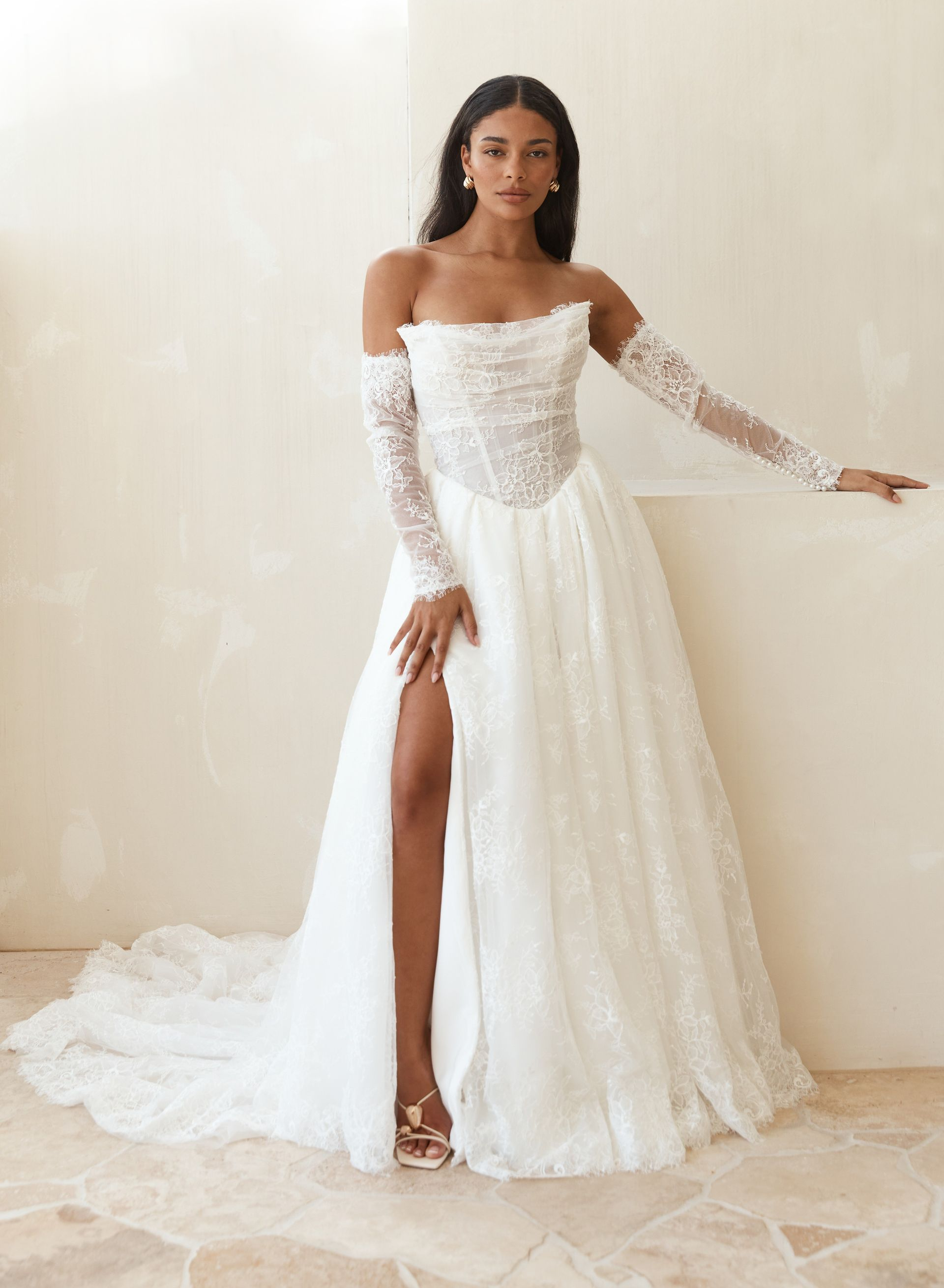 A woman in a white wedding dress is standing in front of a fireplace.