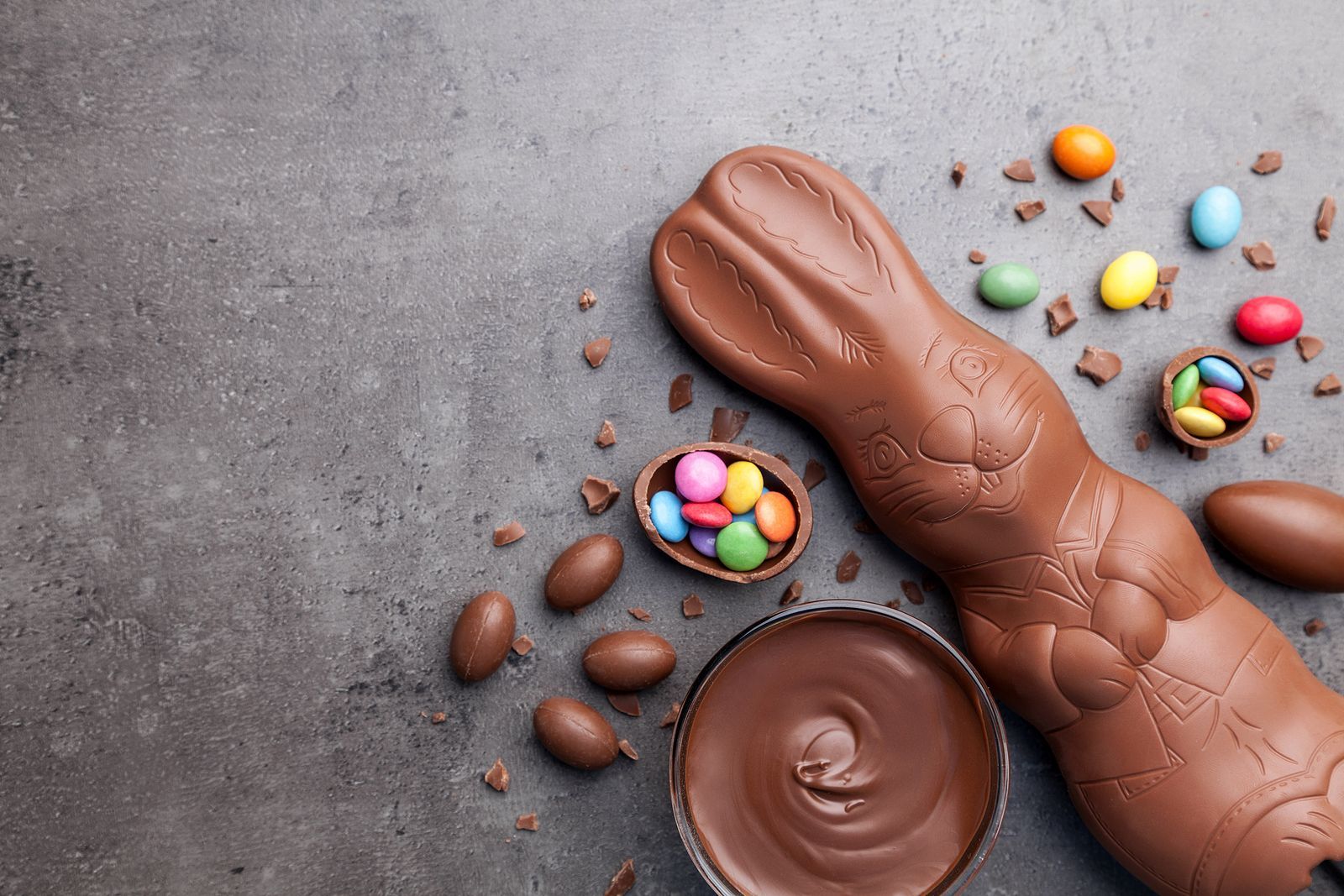 A chocolate bunny surrounded by easter eggs and chocolate sauce on a table.