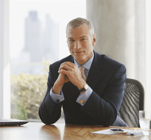 A businessman with his elbows resting on his desk and looking intently at the camera