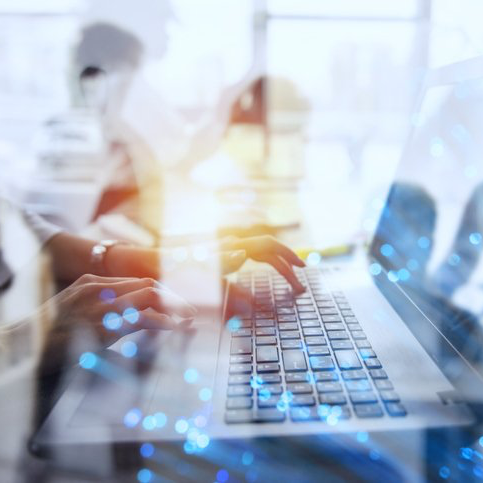 A close up of hands typing on a laptop keyboard in an illuminated room