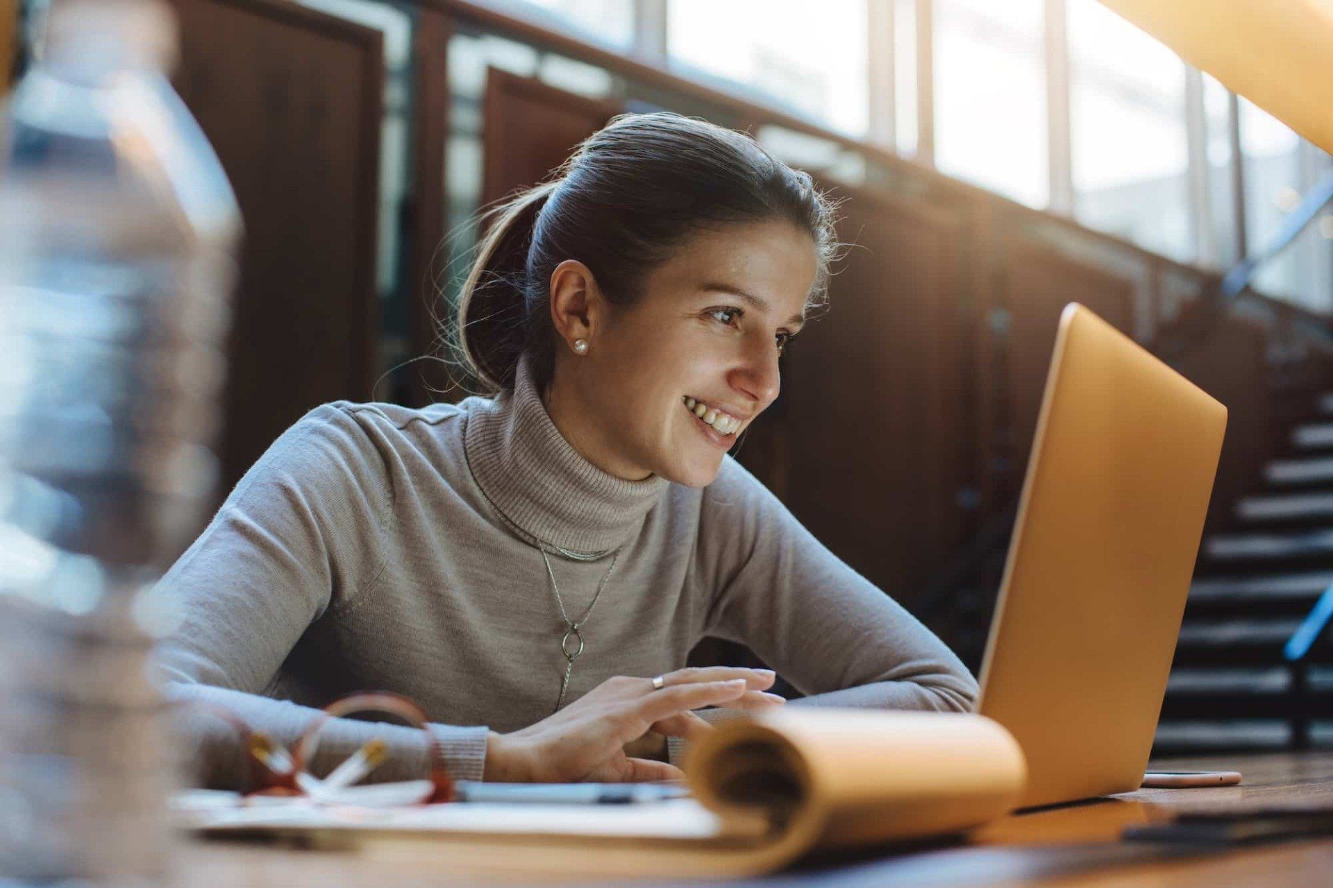 A woman smiling at her laptop screen