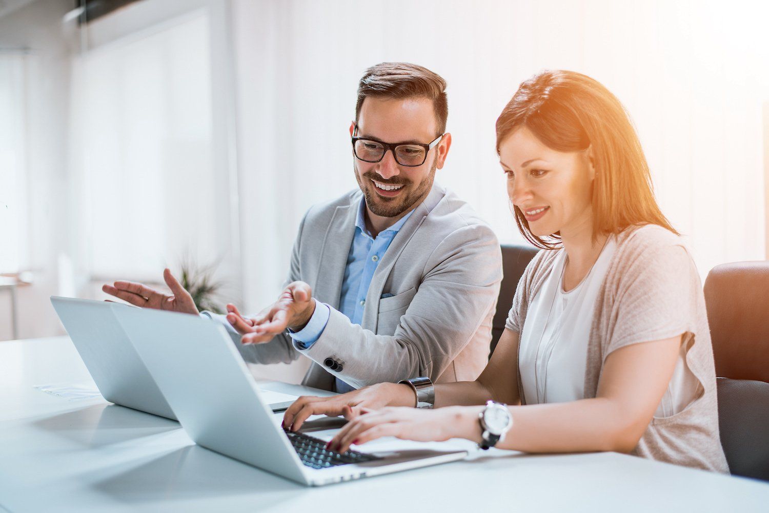 A man and a woman talking and sitting at a table with their laptops