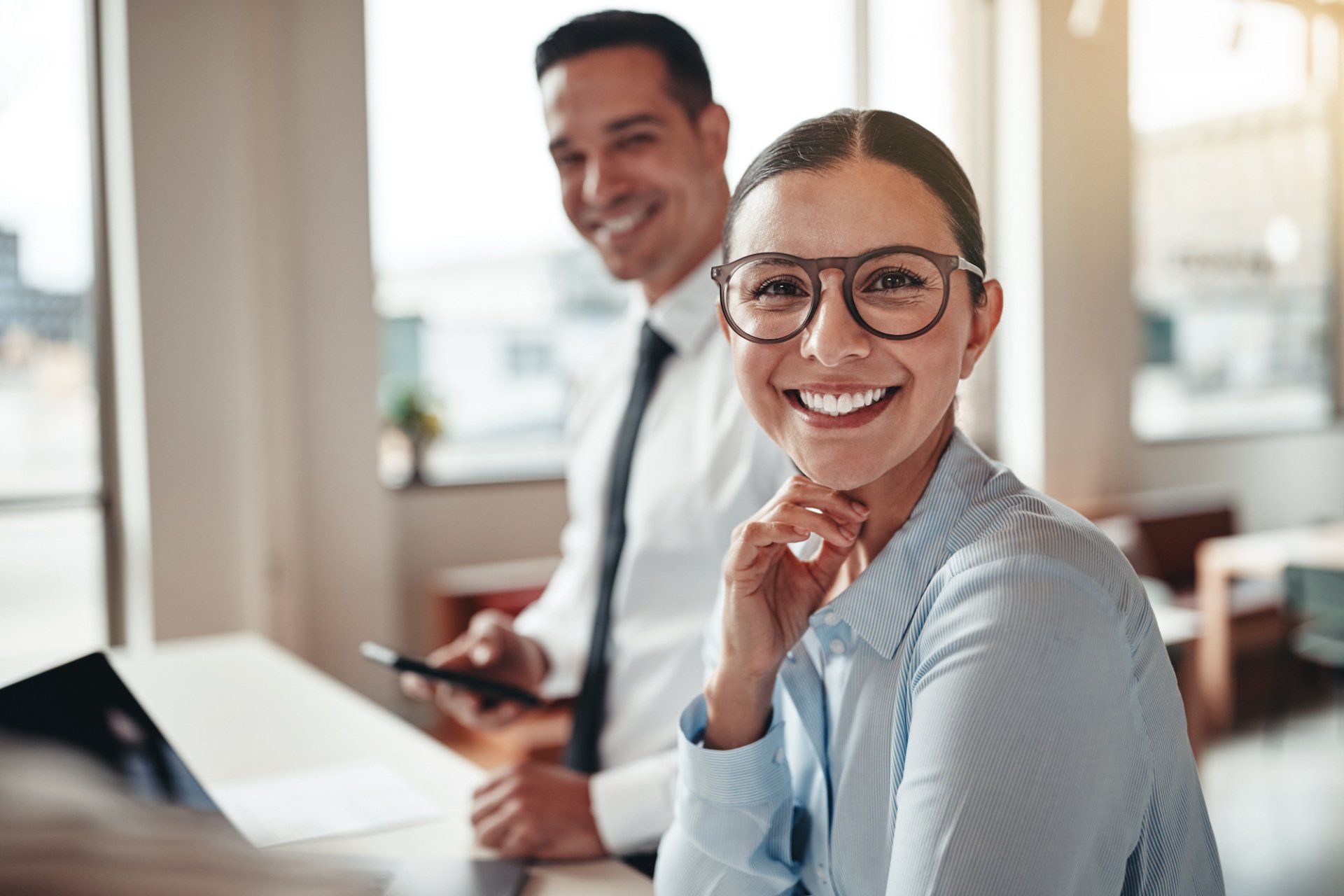 Two people smiling at the camera in a bright office