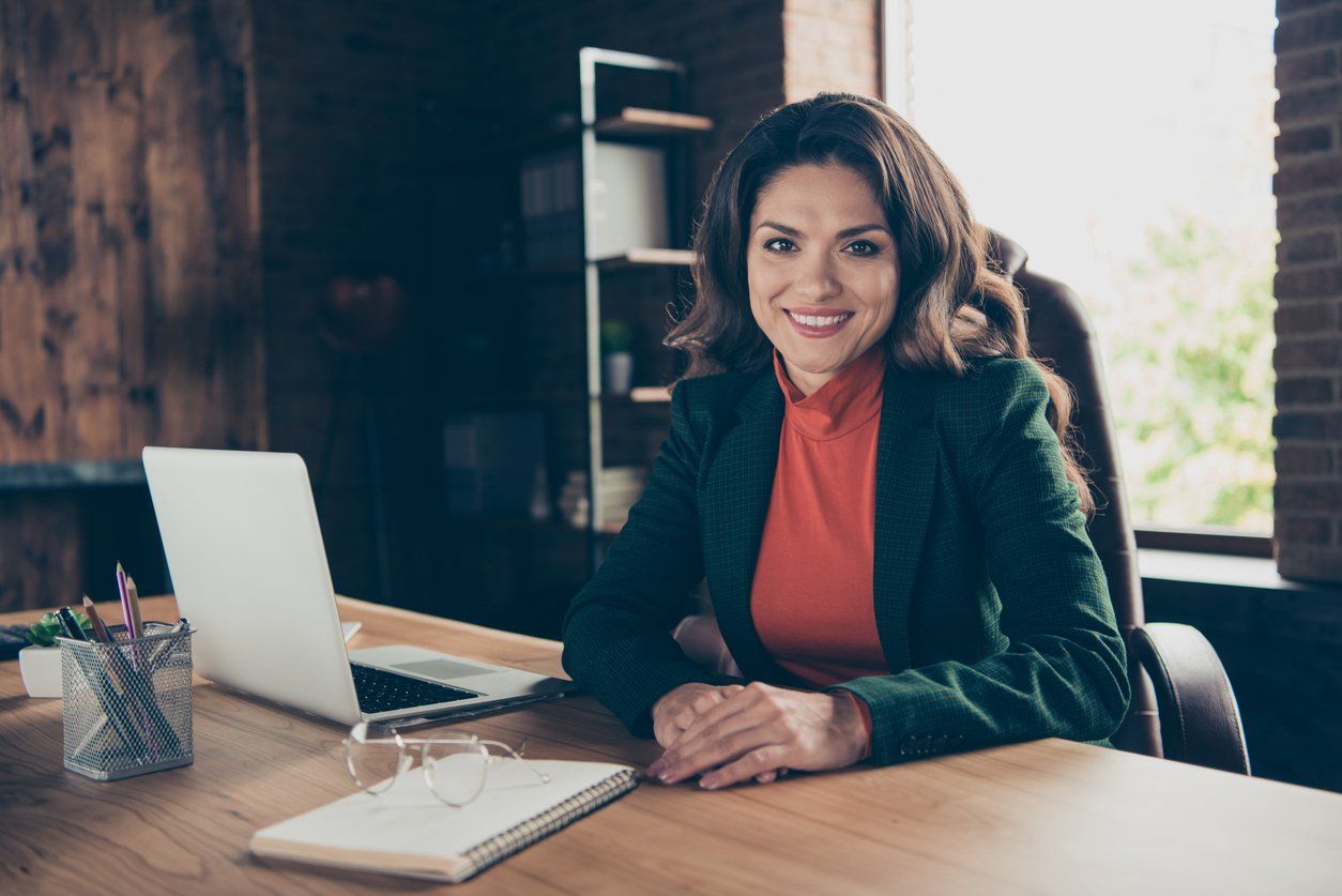 A woman in a red shirt and coat sits in her office