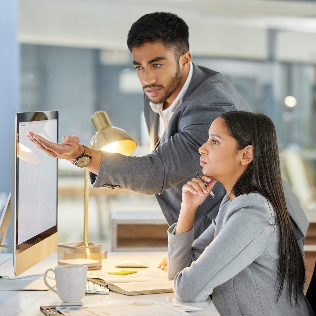 A man gestures to a computer screen while a woman watches as they collaborate in a business setting