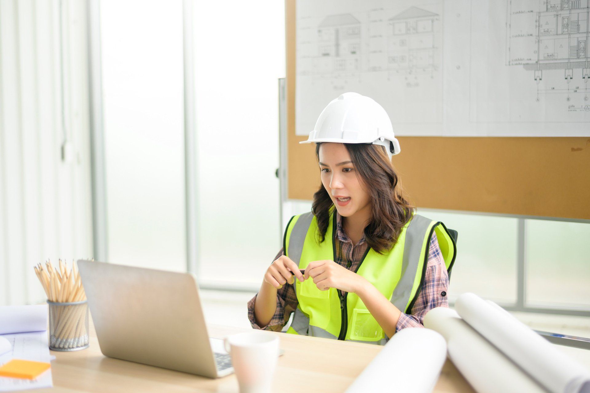 A woman in a hard hat and vest speaking during a virtual conference