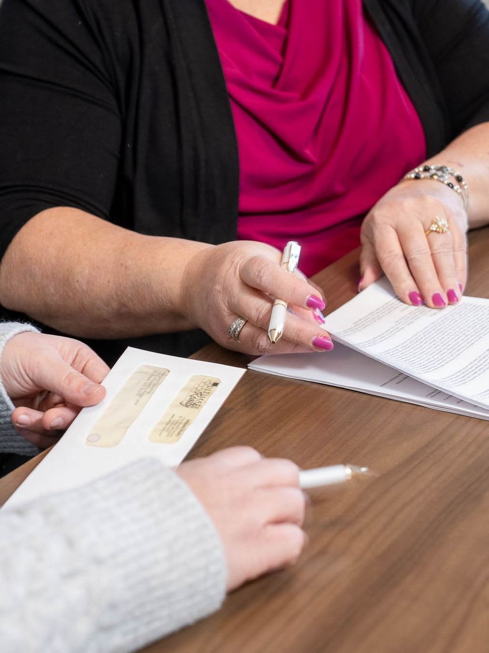 image of two women sitting at a conference table, cropped to see only their hands transferring paperwork and signing things
