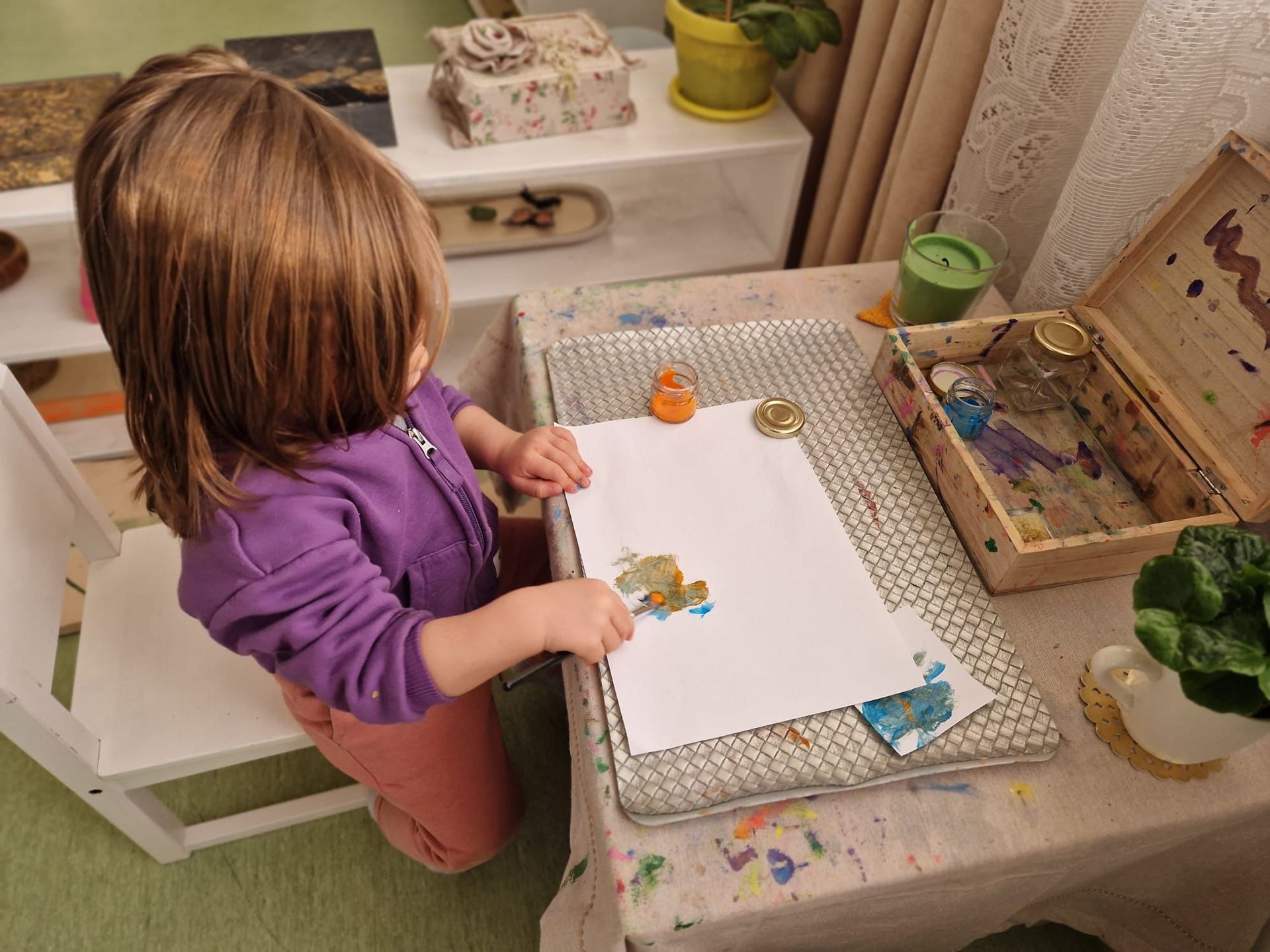 A little girl is sitting at a table playing with paint.