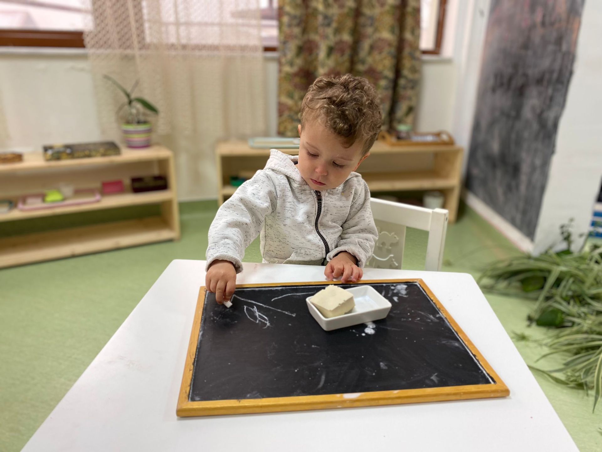 A young boy is sitting at a table playing with a chalkboard.
