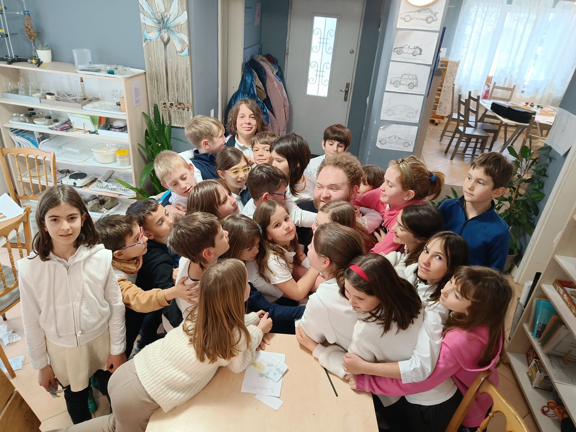 A large group of children are sitting around a table in a room.