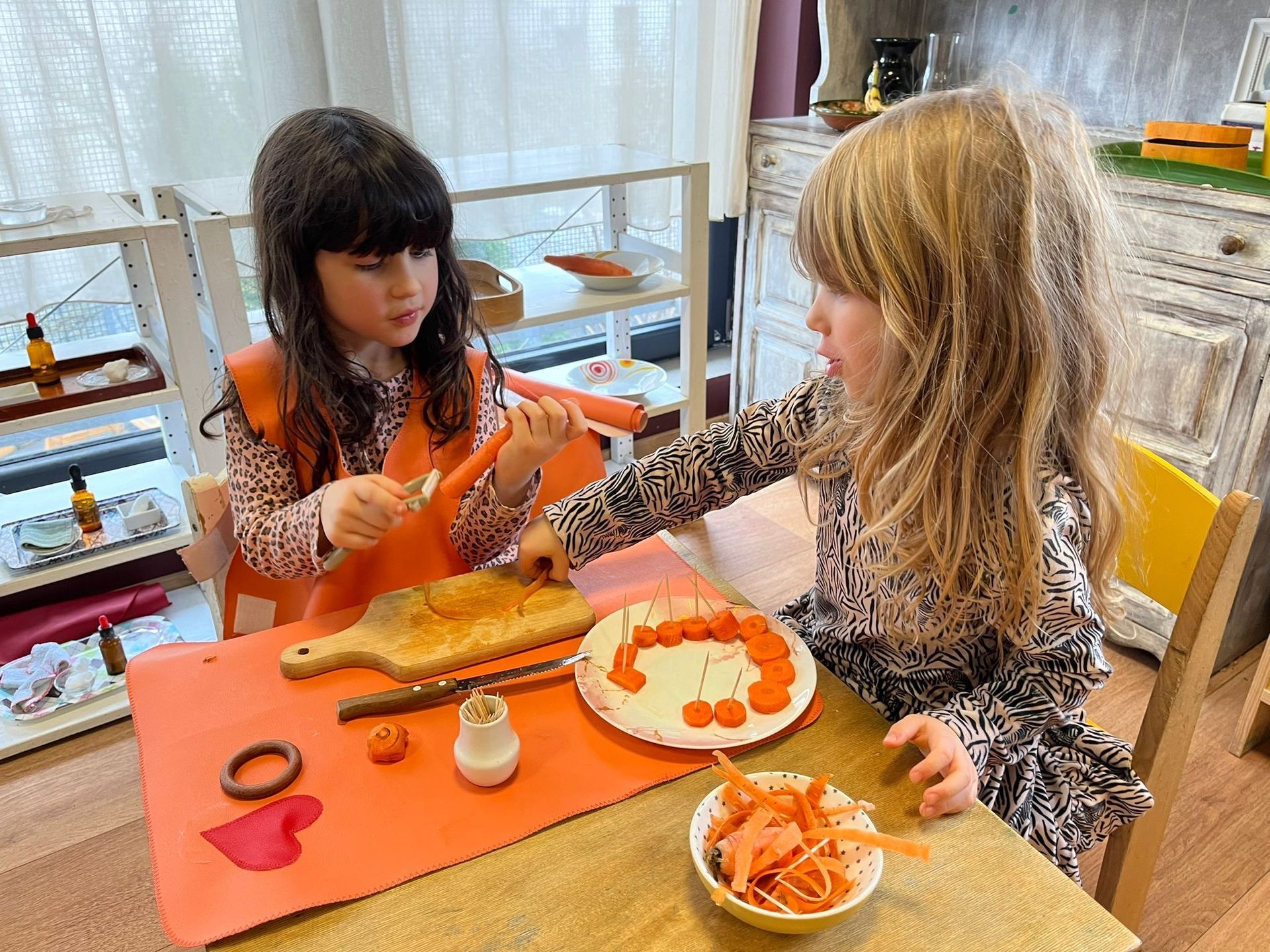 Two little girls are sitting at a table playing with carrots.