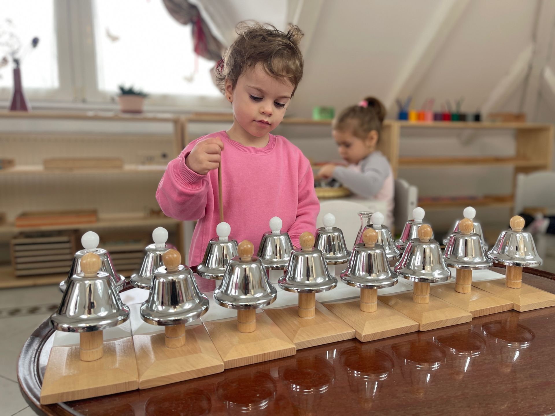 A little girl is playing with a row of bells on a table.