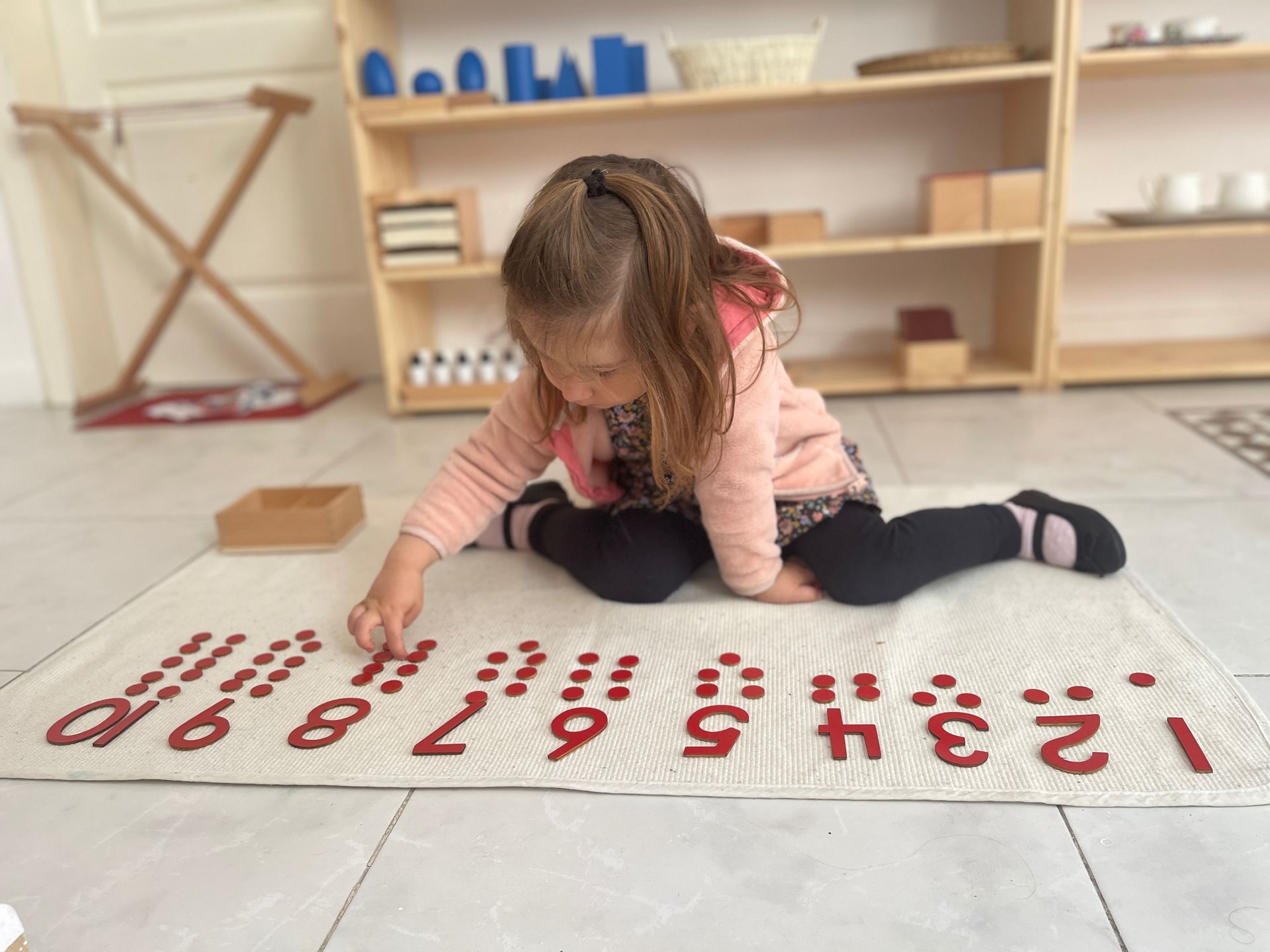A little girl is sitting on the floor playing with numbers