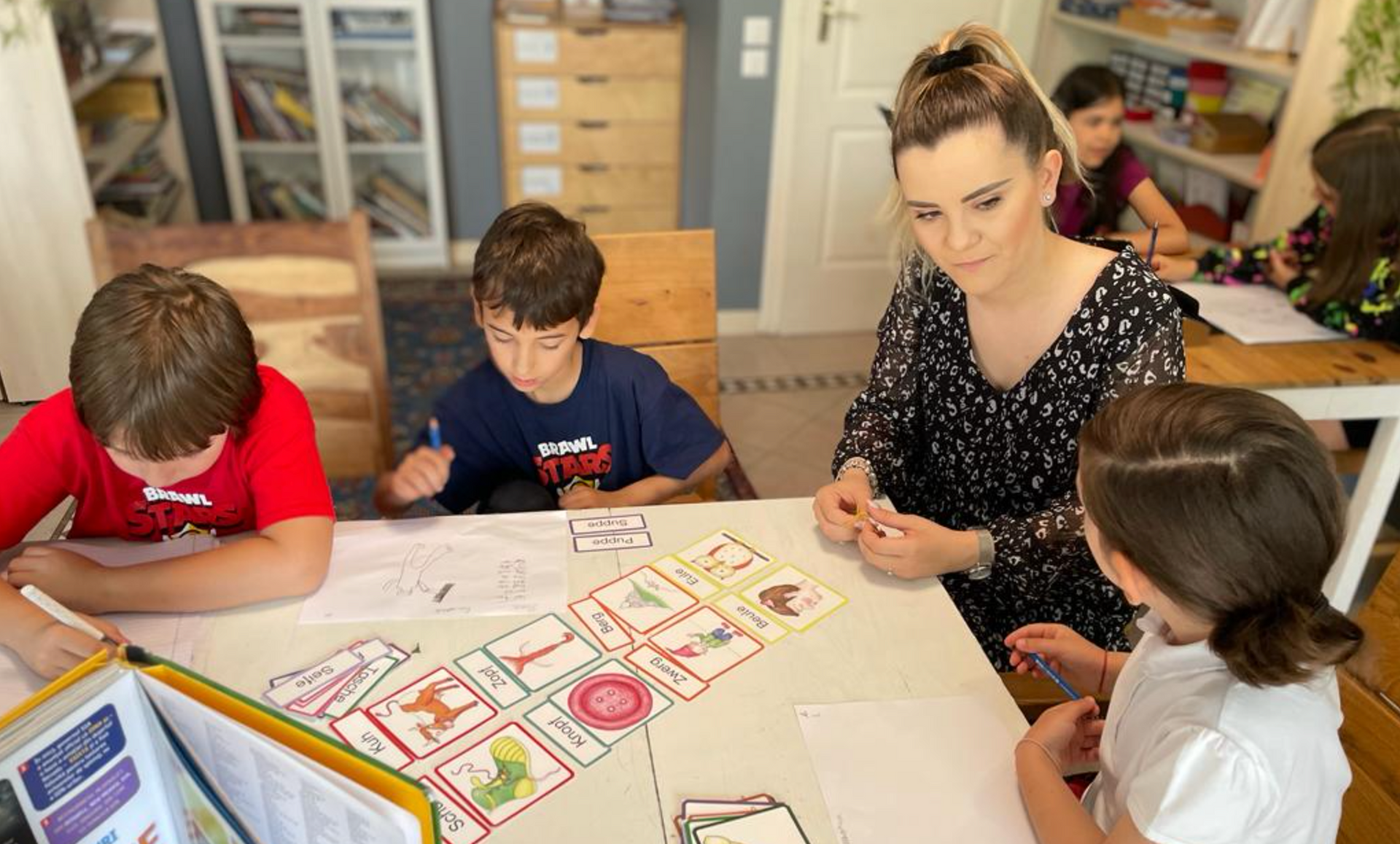 A woman is sitting at a table with three children playing a game.