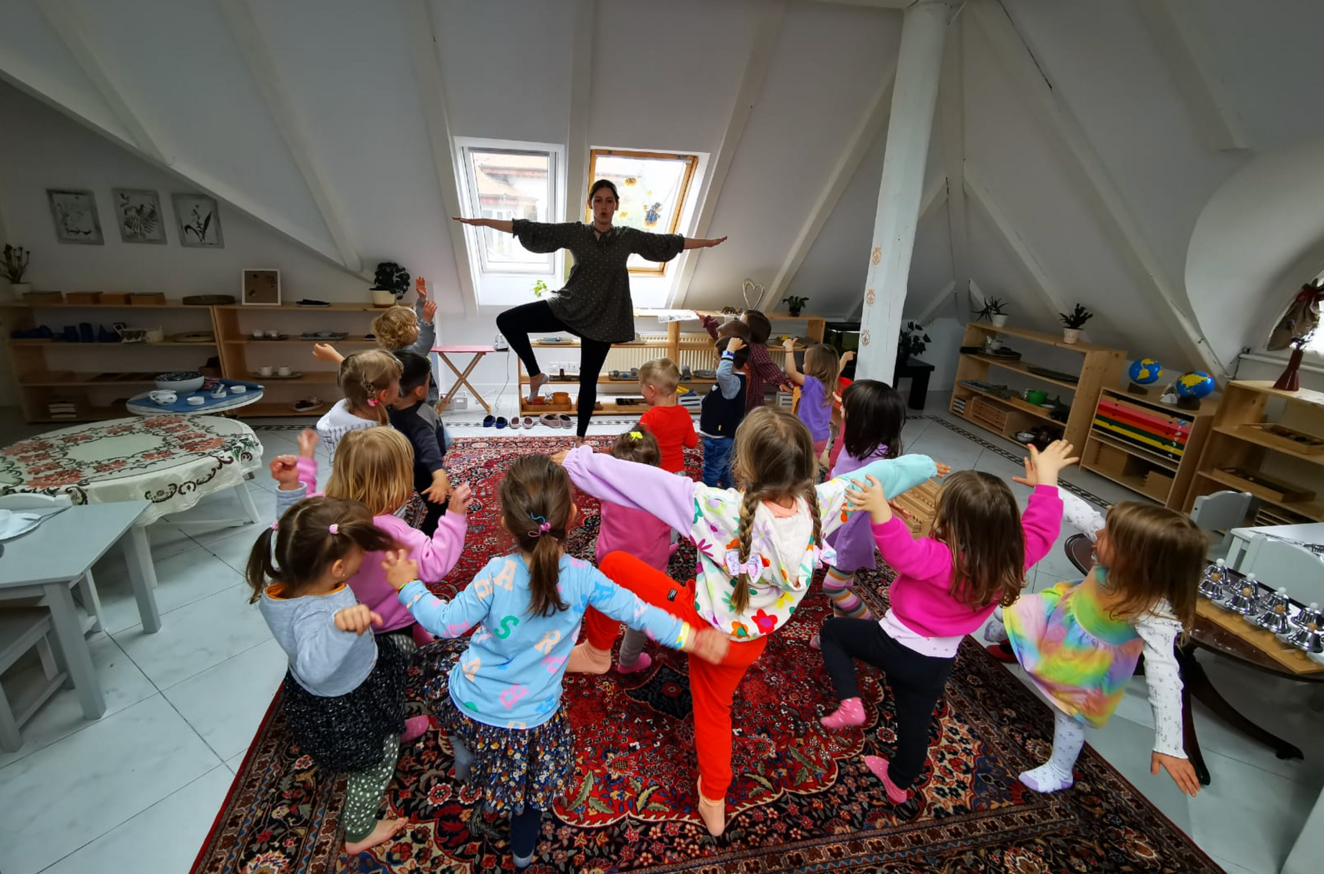A woman is doing yoga with a group of children in a room.