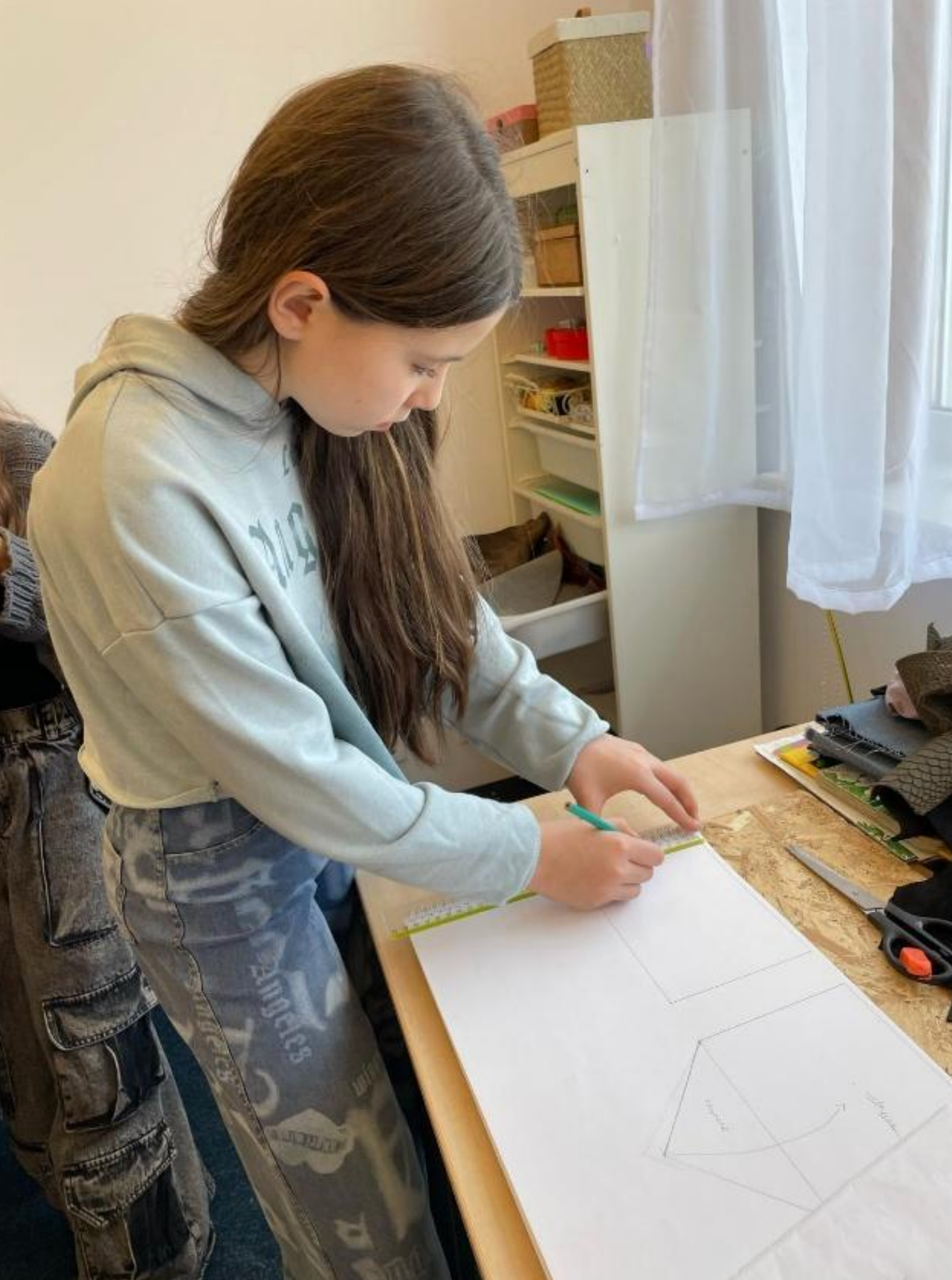 A young girl is sitting at a table drawing on a piece of paper.