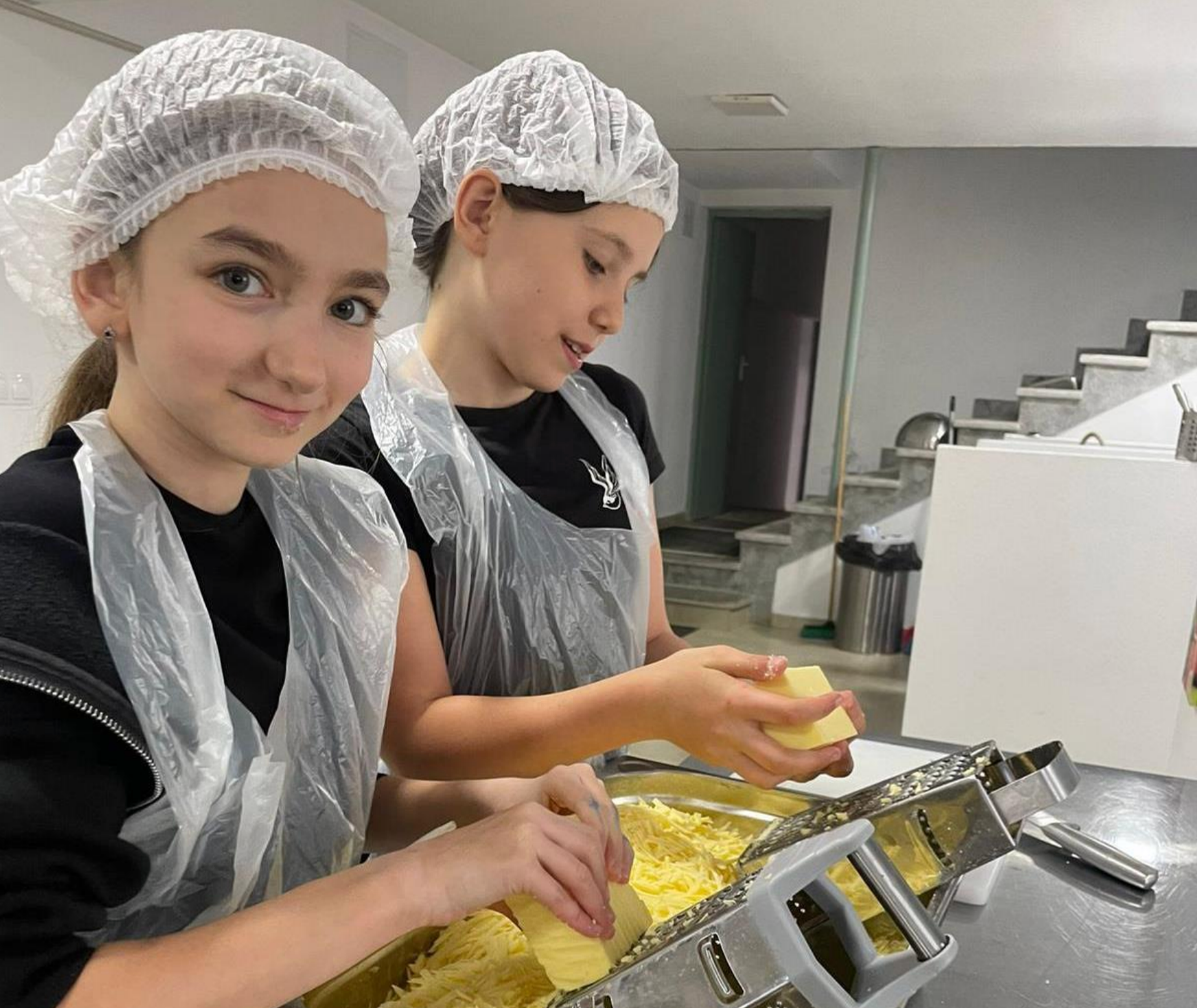 Two girls wearing plastic aprons and hair nets are working in a kitchen