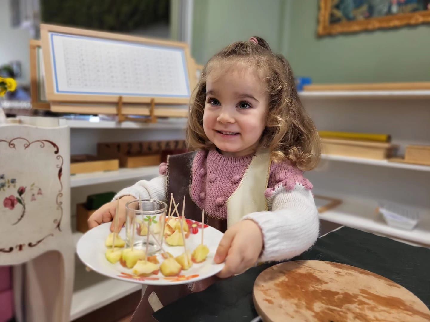 A little girl is holding a plate of apples on toothpicks.