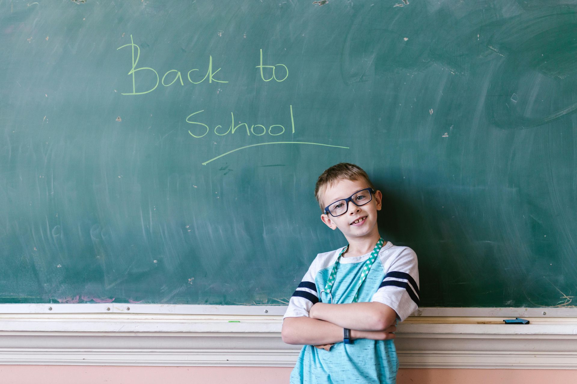 A young boy is standing in front of a blackboard with the words `` back to school '' written on it.