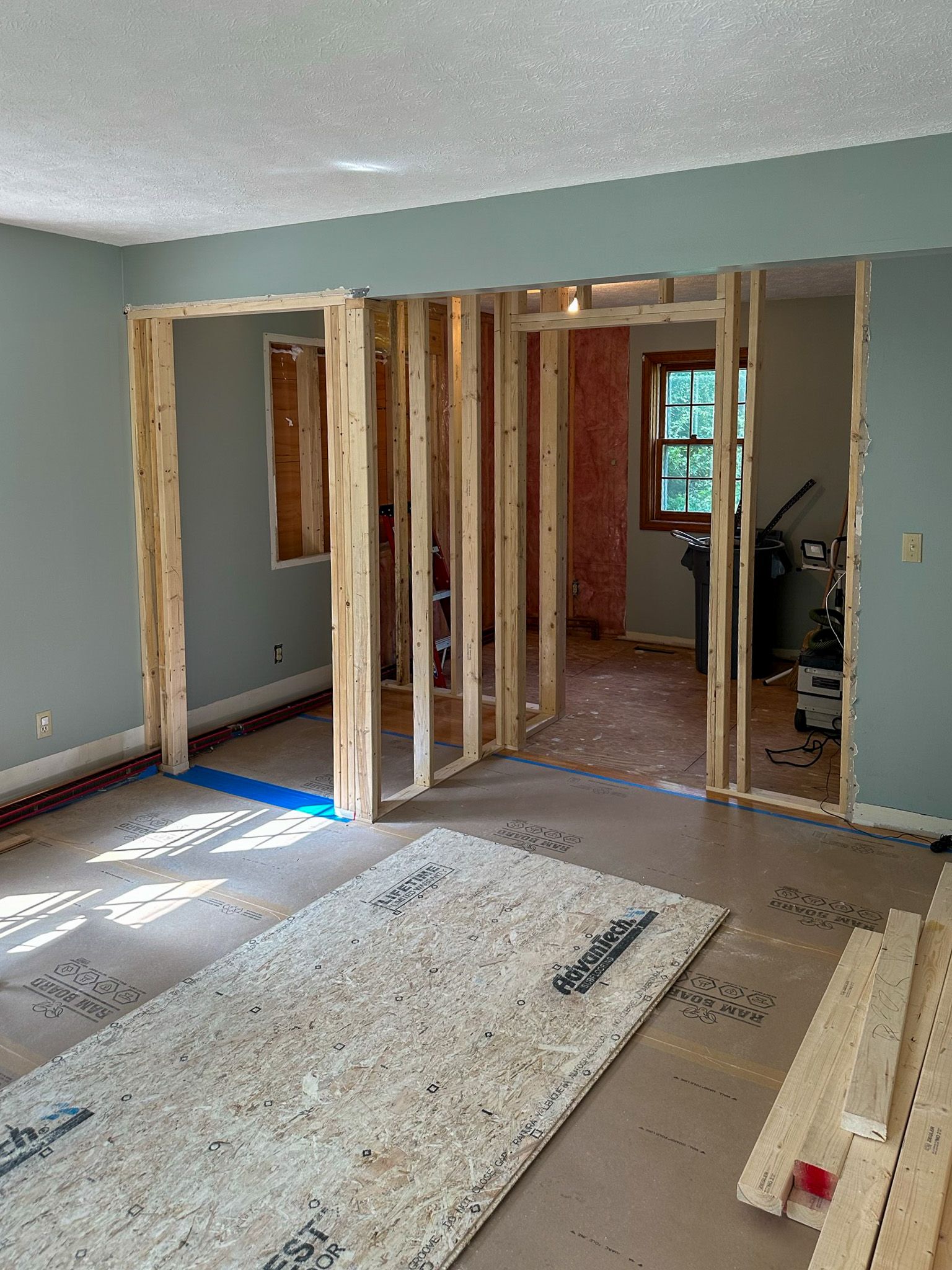 Interior view of a room under construction, showing exposed wooden framing for a new wall with doorways and light blue walls.
