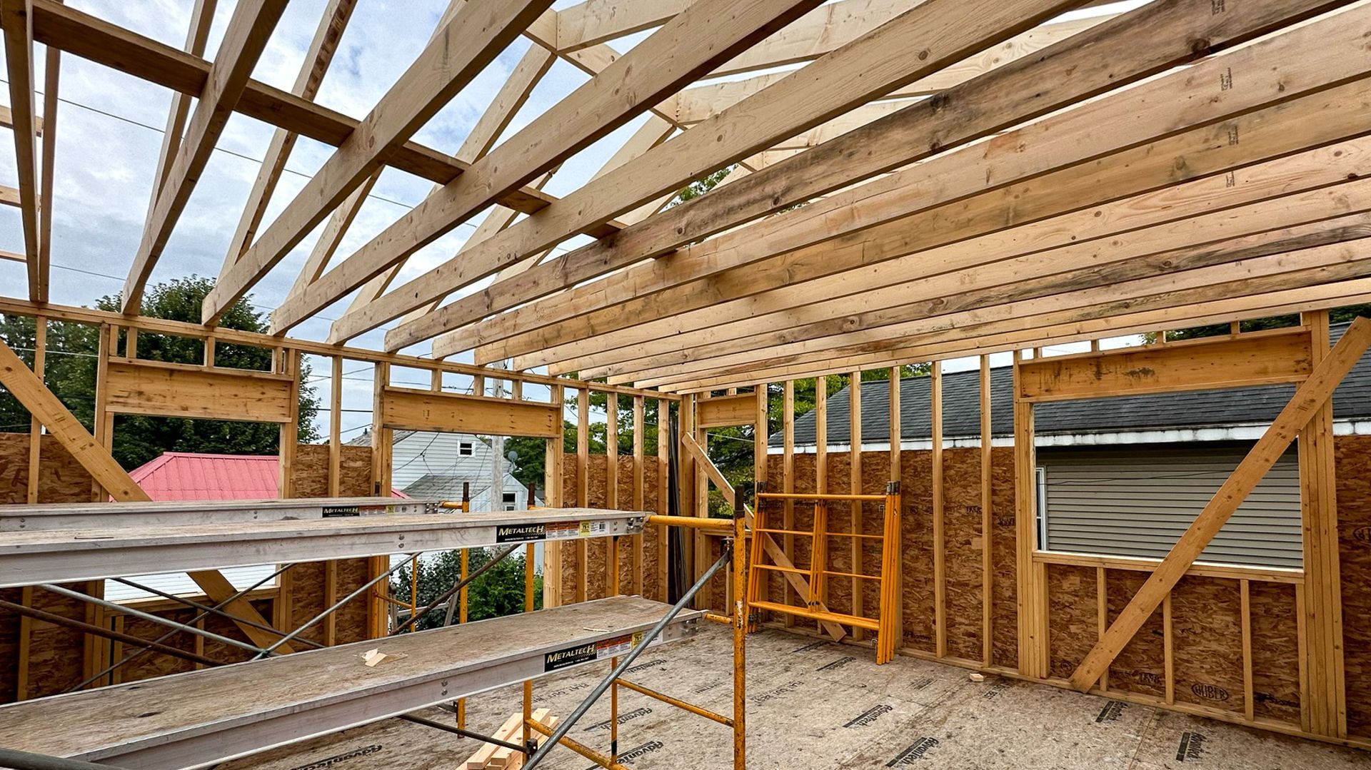 Wooden framework of a building under construction, showing roof beams, walls, and scaffolding.