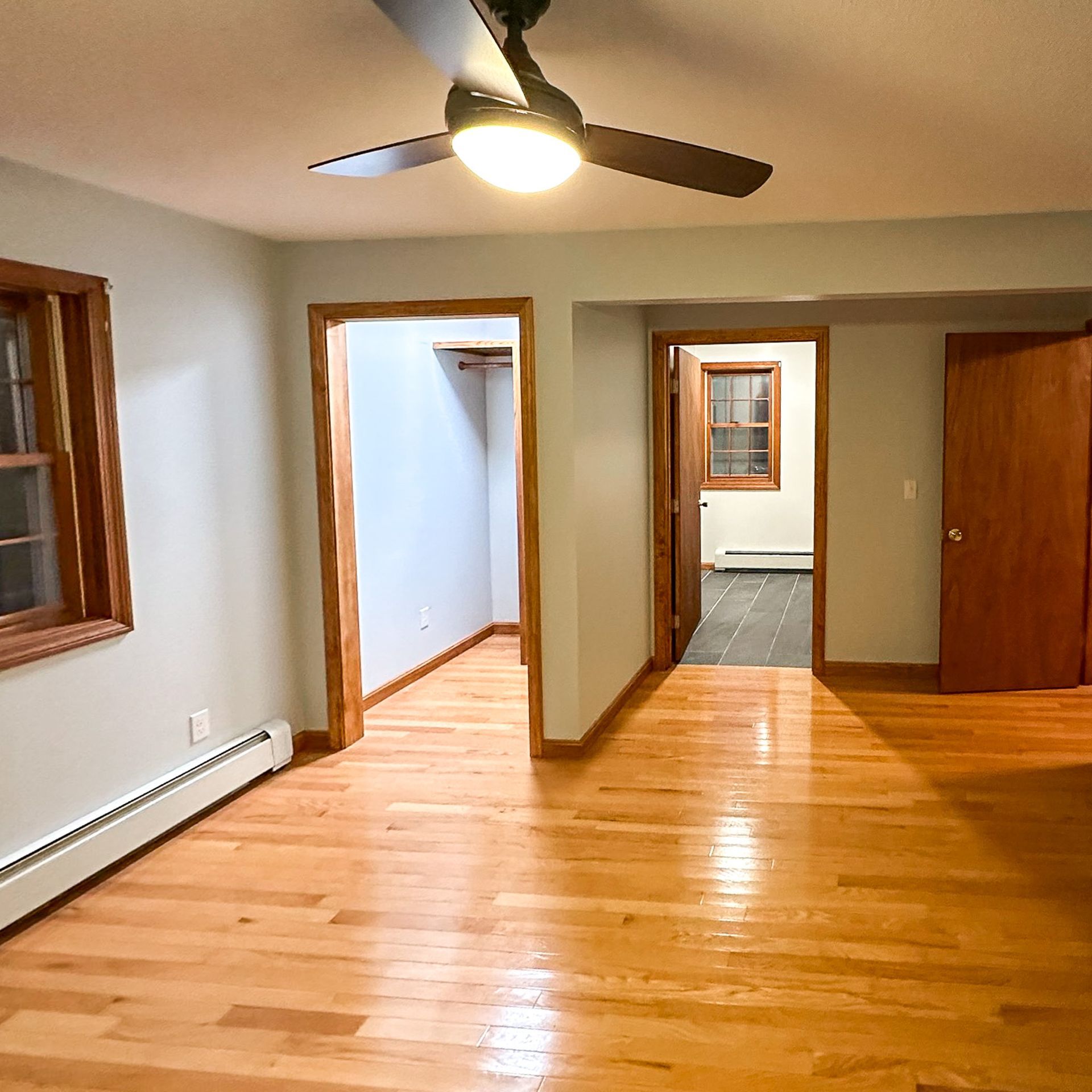 A room with hardwood floors, two doorways, and a ceiling fan. One doorway leads to a closet, and the other leads to another room with a window.