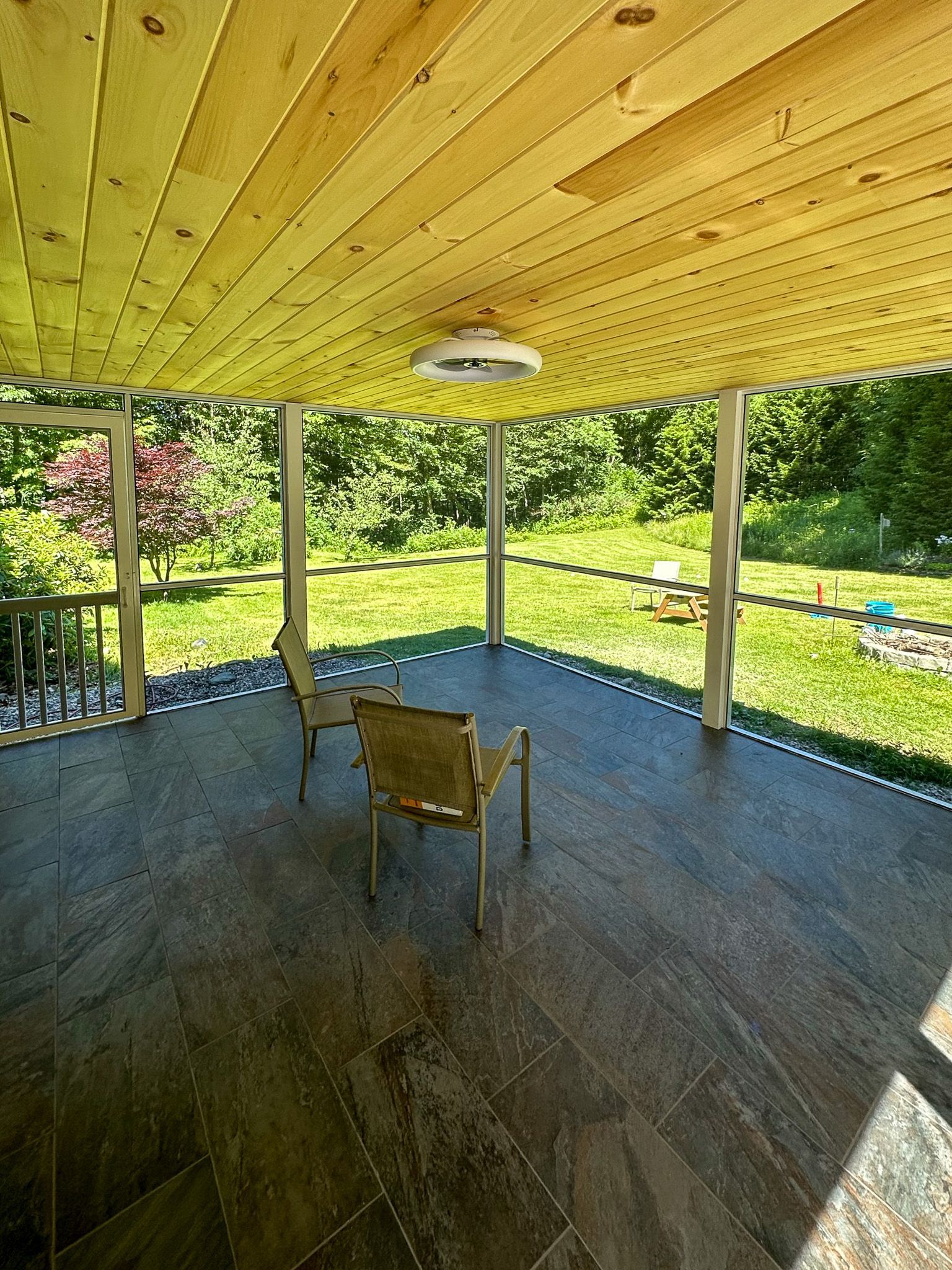 Covered porch with wood ceiling and tile floor; two chairs face a green yard.