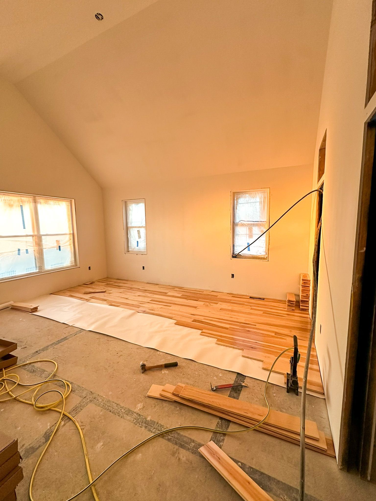 Interior of a room under construction with wood flooring being installed. Light floods in from windows, and tools are scattered about.