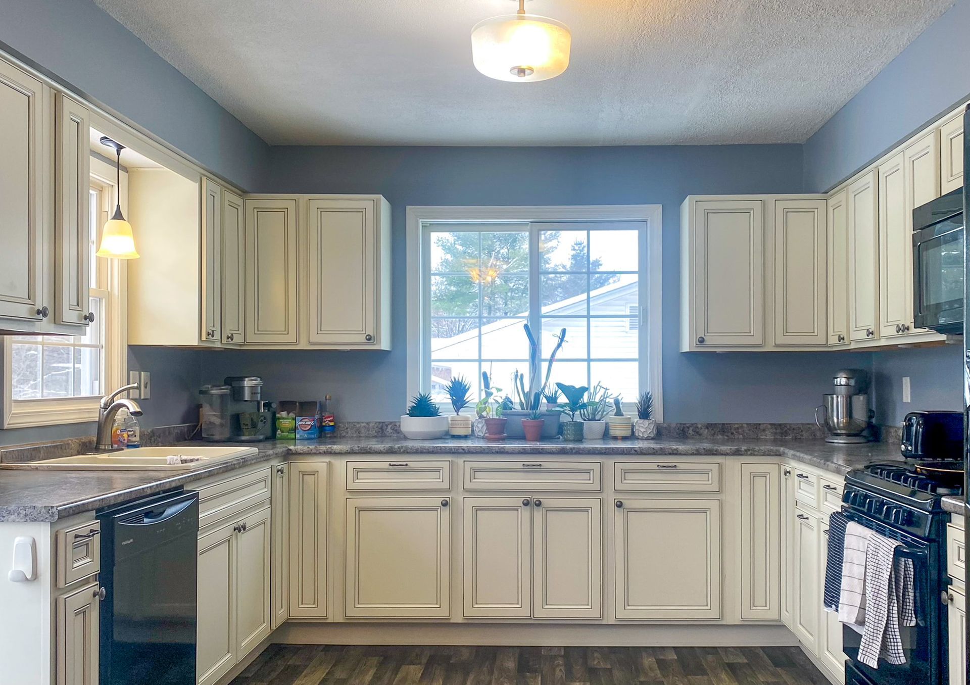 U-shaped kitchen with off-white cabinets, a window with a winter scene, and light blue walls. Dark countertop and stove.
