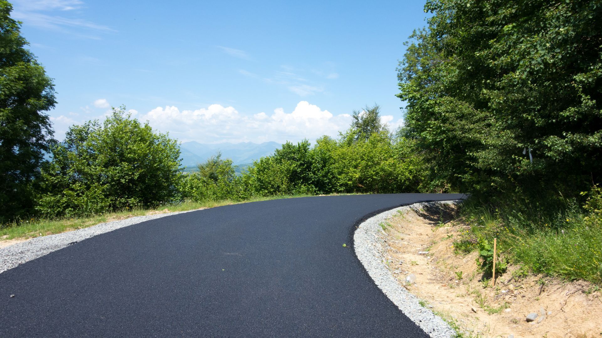 A curvy road with trees on both sides and a blue sky in the background