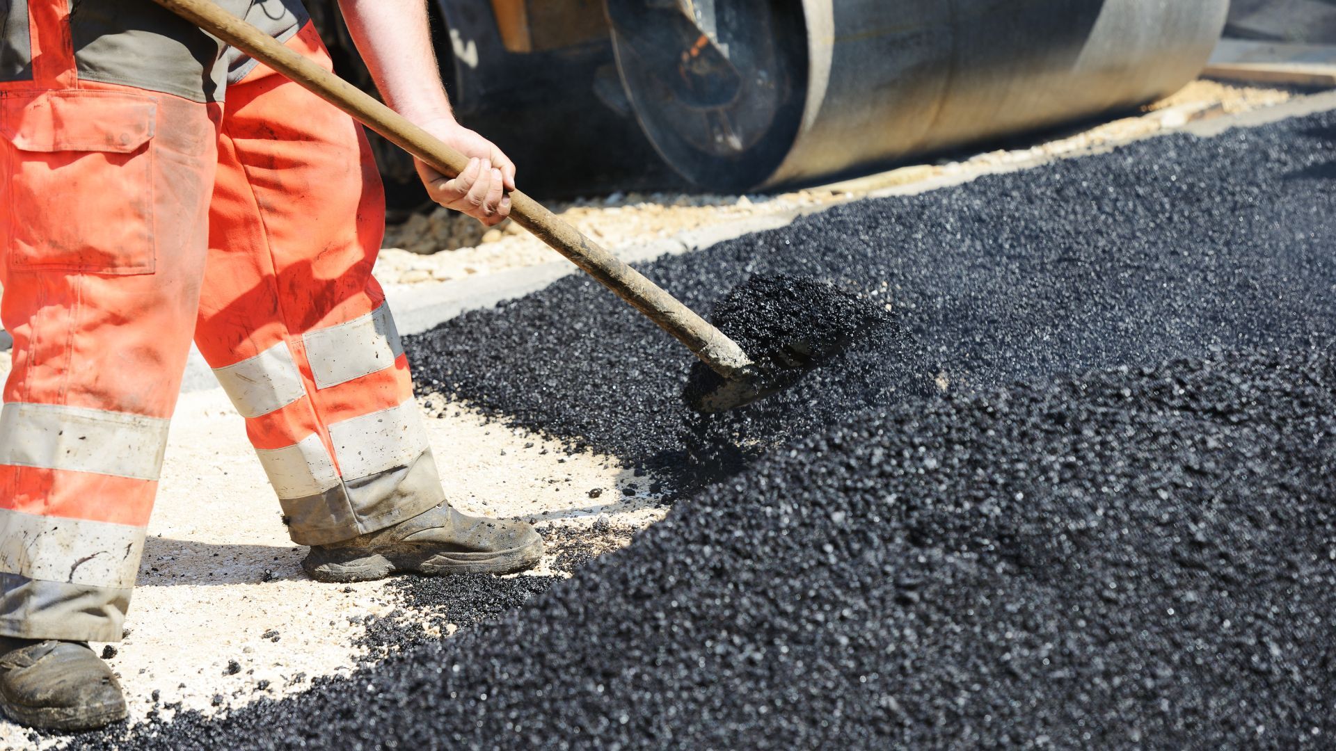 A man is spreading asphalt on a road with a shovel.