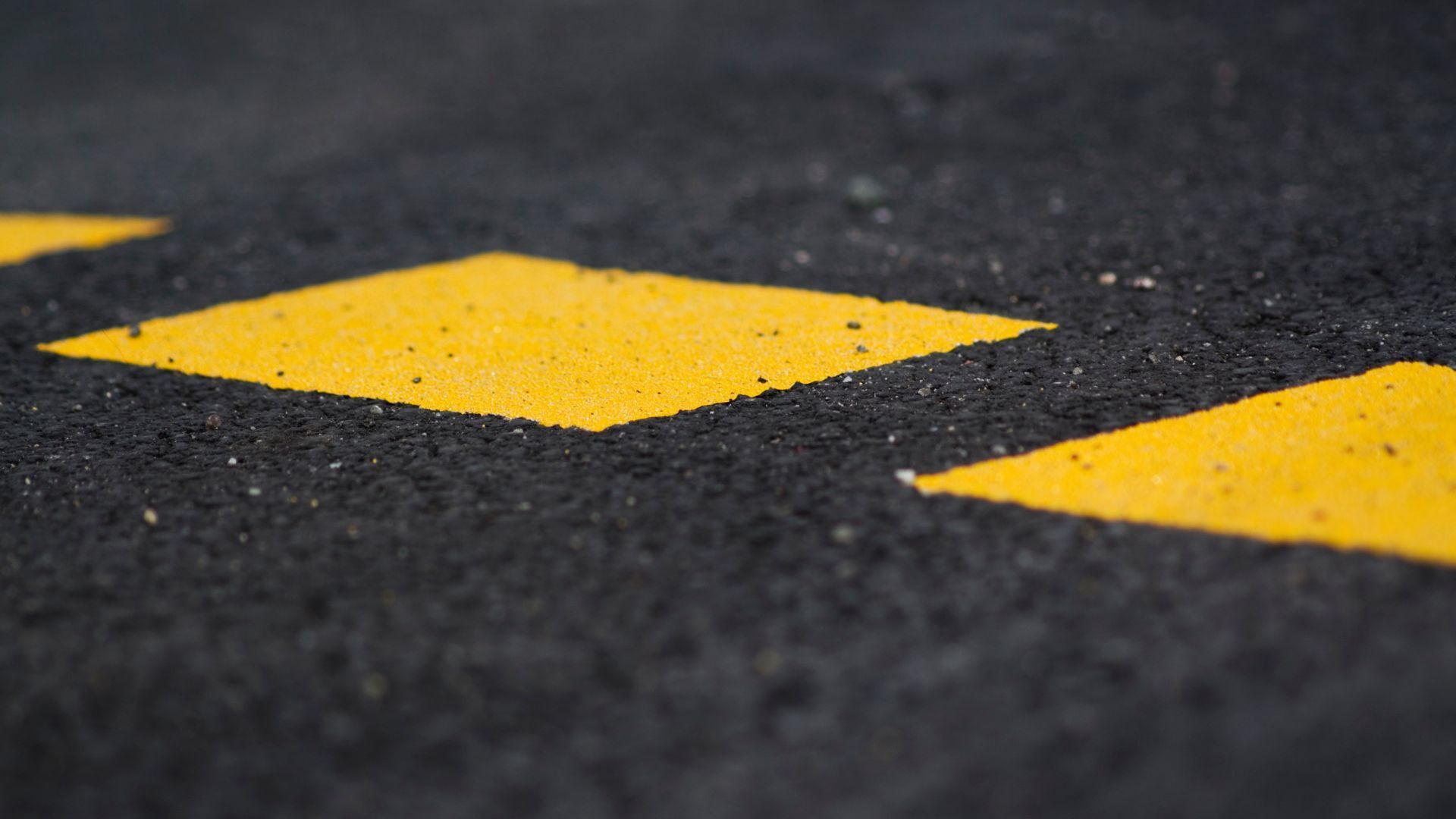 A close up of a yellow arrow on a black road.