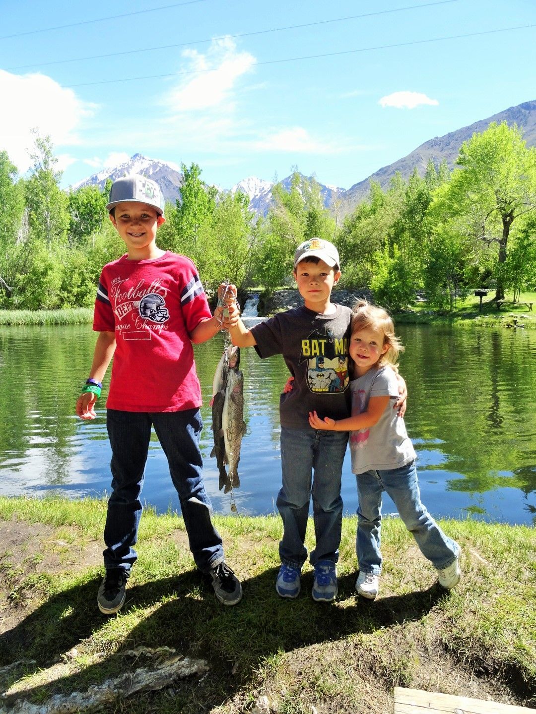 A boy and a girl are holding a fish in front of a lake.