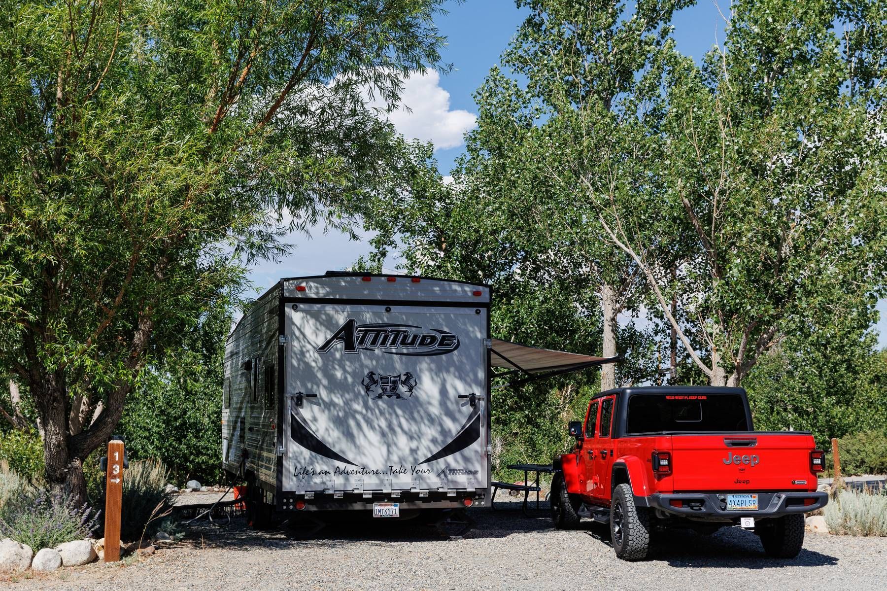 A red truck is towing a trailer in a parking lot.