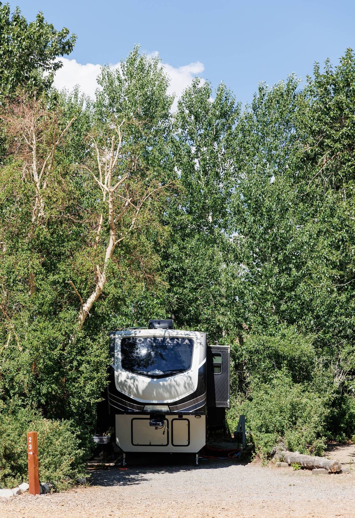 A rv is parked in a gravel area surrounded by trees.