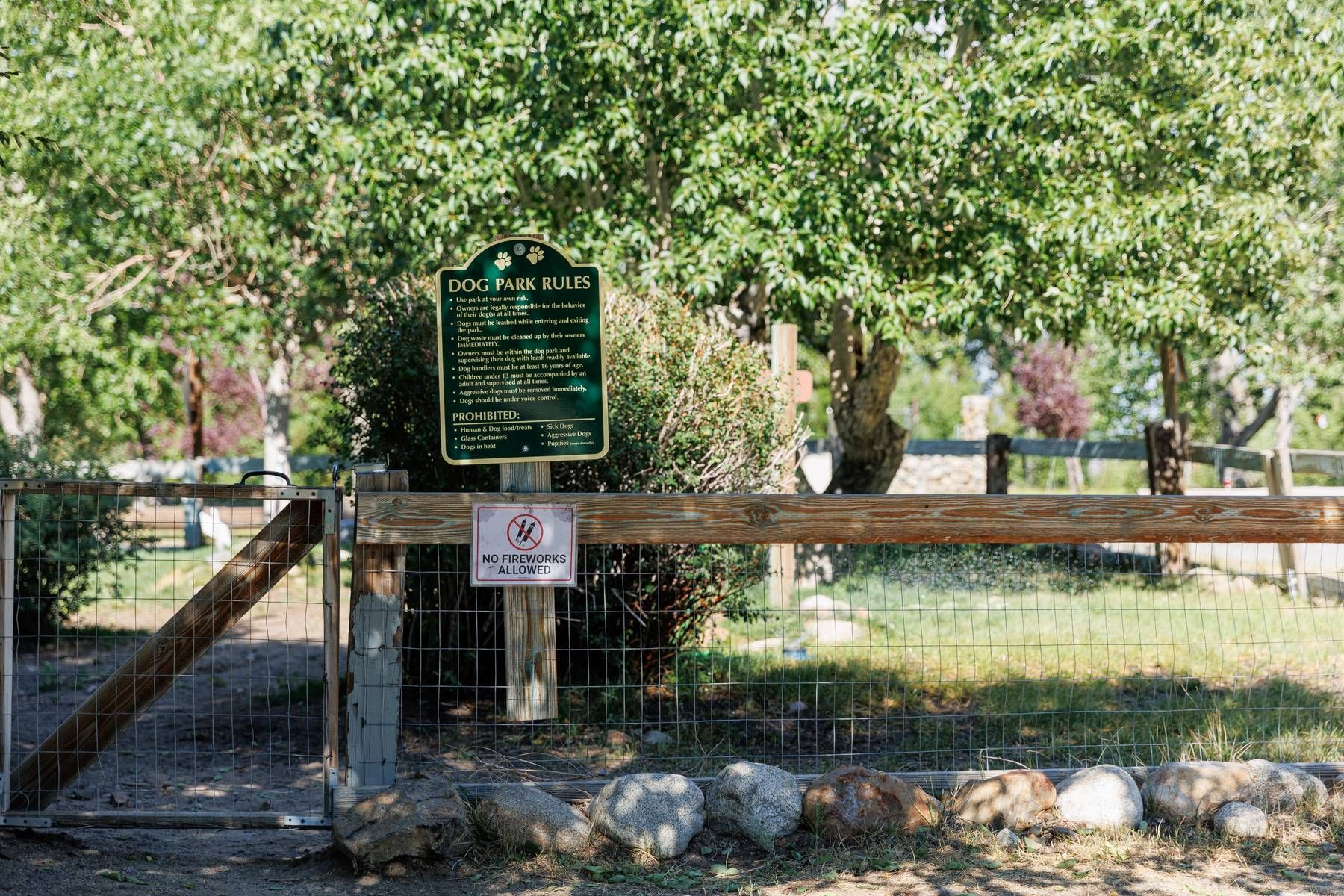 A wooden fence with a sign on it and trees in the background.