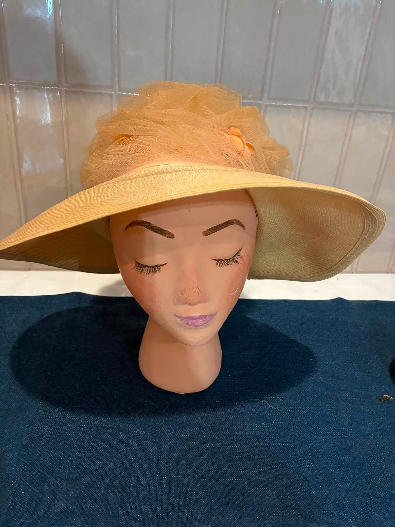 Mannequin head wearing a wide-brimmed straw hat on a dark blue surface against tiled wall.