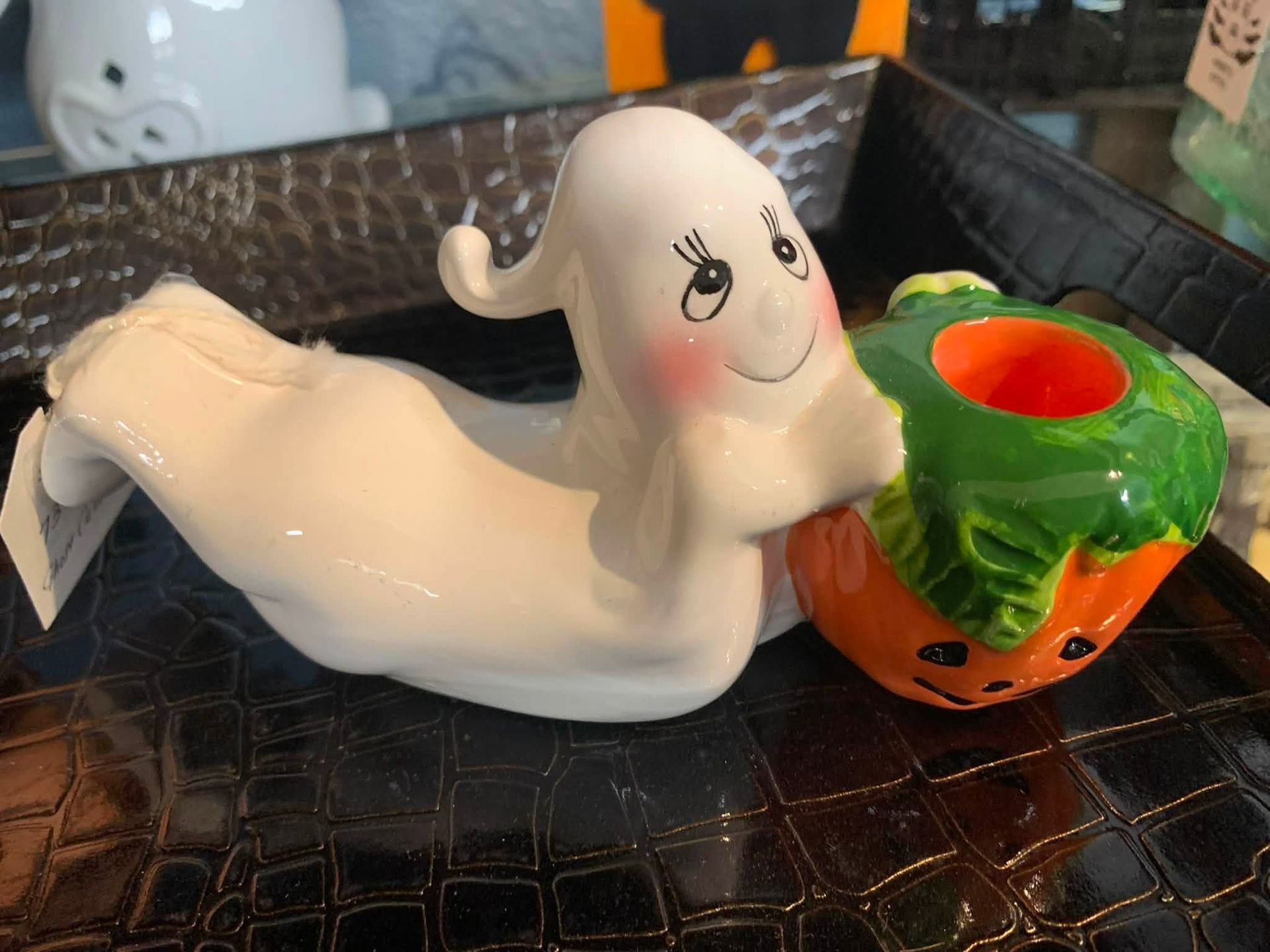 White ceramic ghost figurine beside a small jack-o'-lantern cup on a dark textured surface