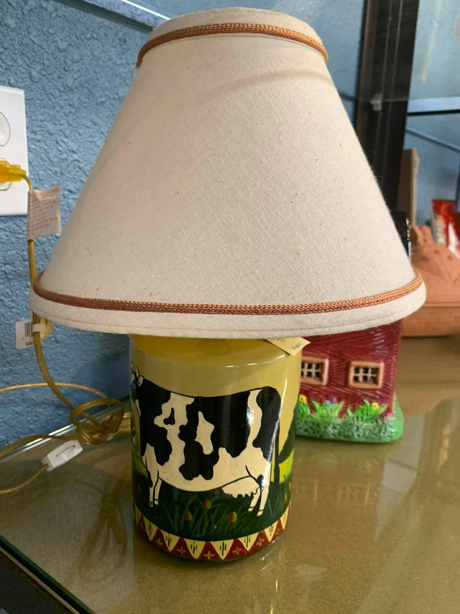 Cow-patterned lamp with cream shade and red trim on a glass table.