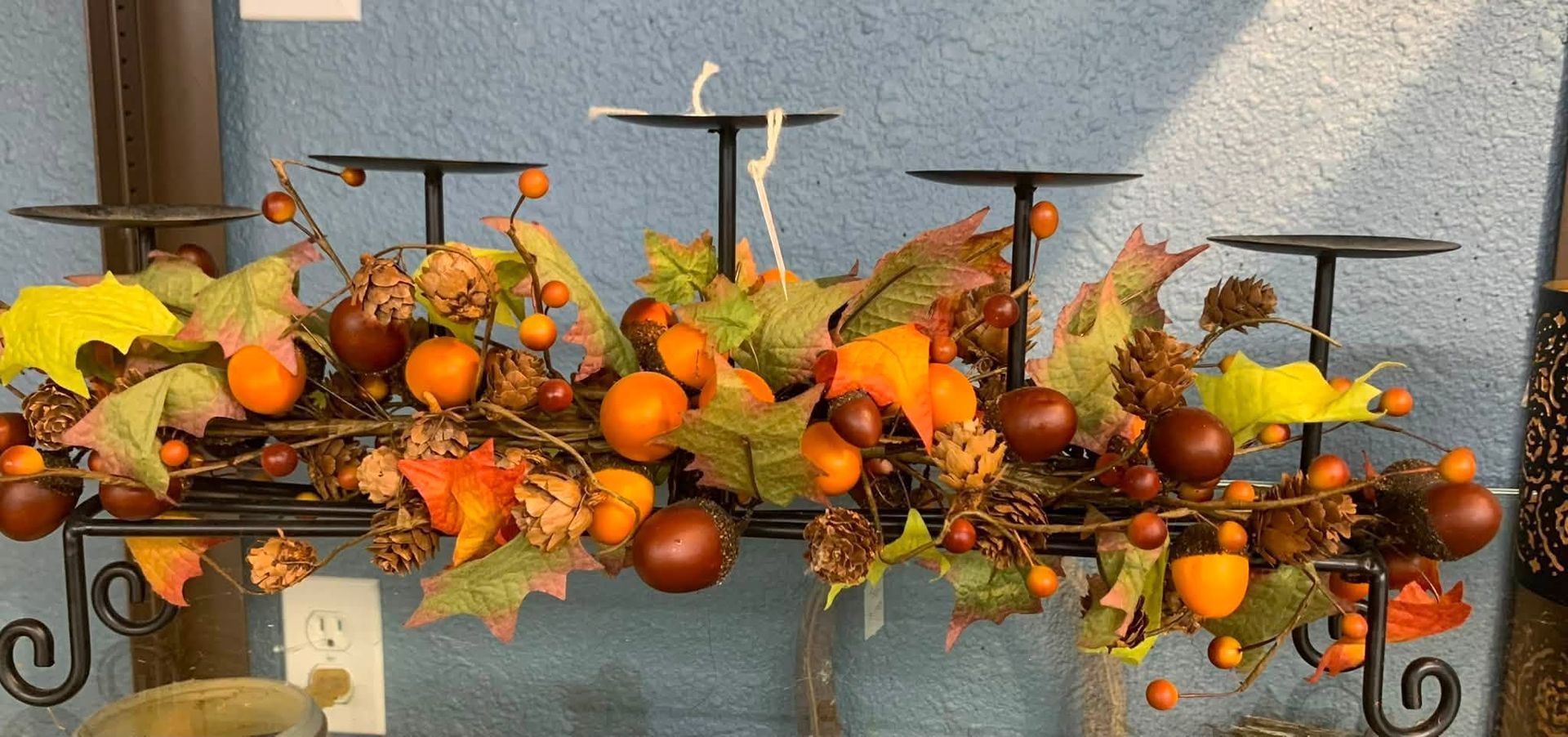 Decorative metal planter filled with orange, yellow, and brown autumn fruits and leaves on a windowsill
